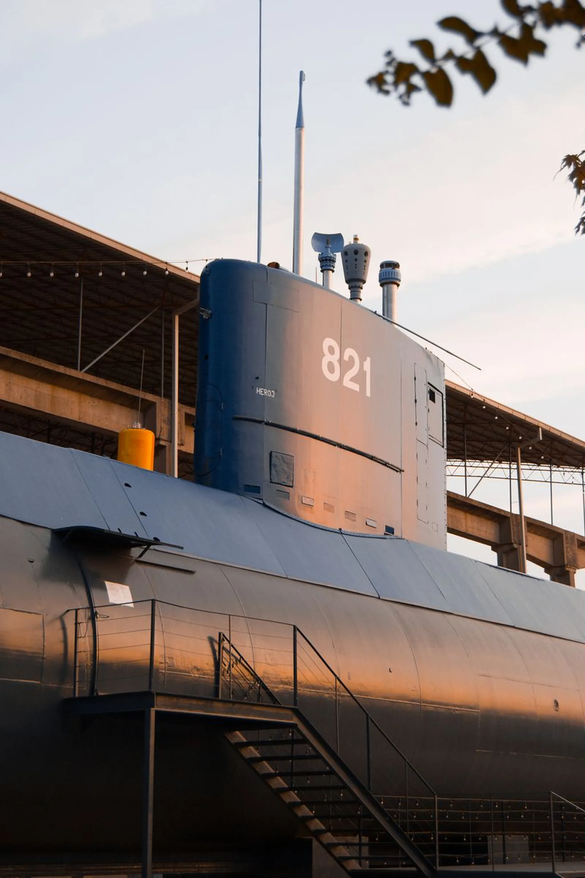 Retired military submarine numbered 821 on display with conning tower, periscopes, and boarding stairs at golden hour