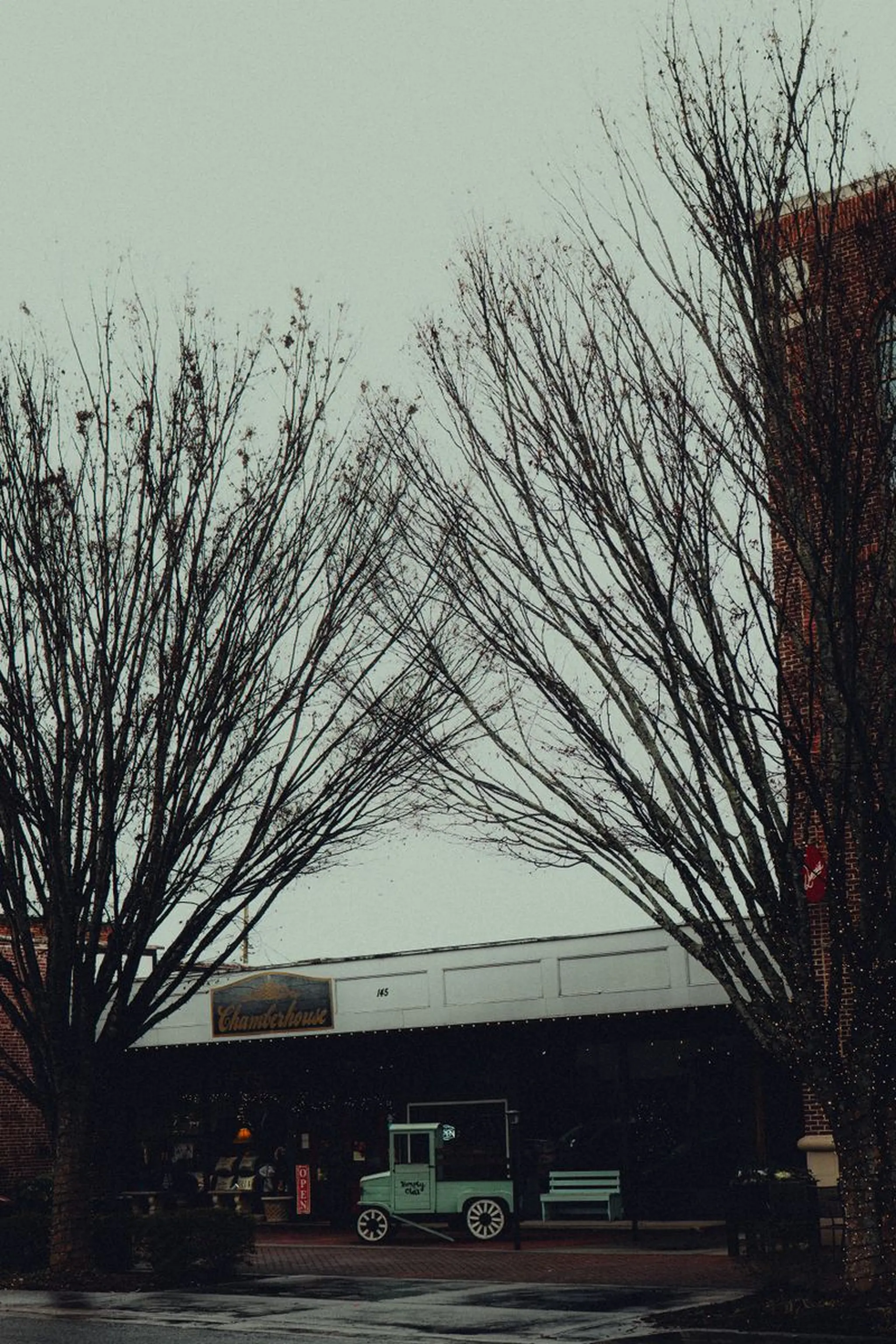 Vintage mint-green truck parked outside a brick storefront with a Chamberhouse sign, framed by bare winter trees under a gray sky