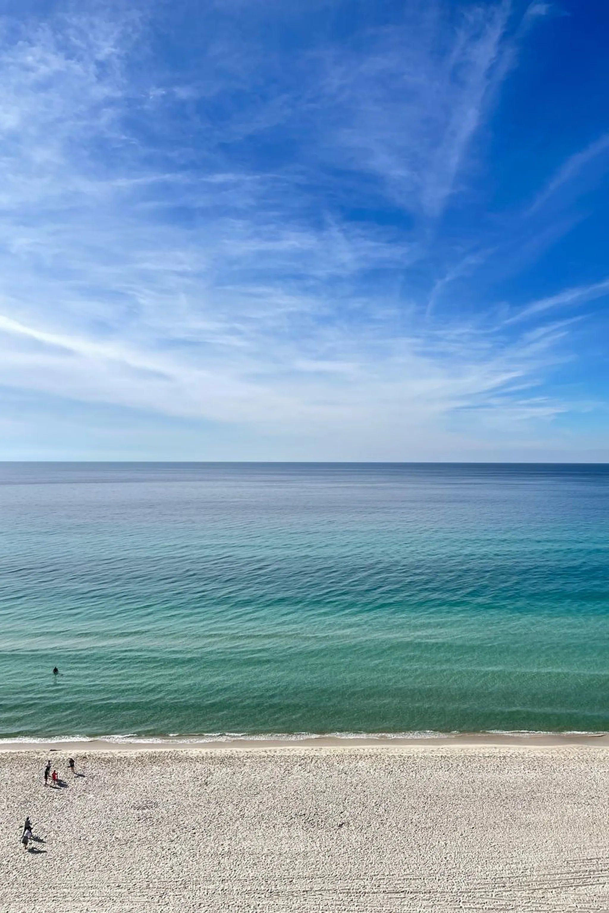 Elevated view of a wide sandy beach meeting turquoise ocean under a bright blue sky with wispy clouds