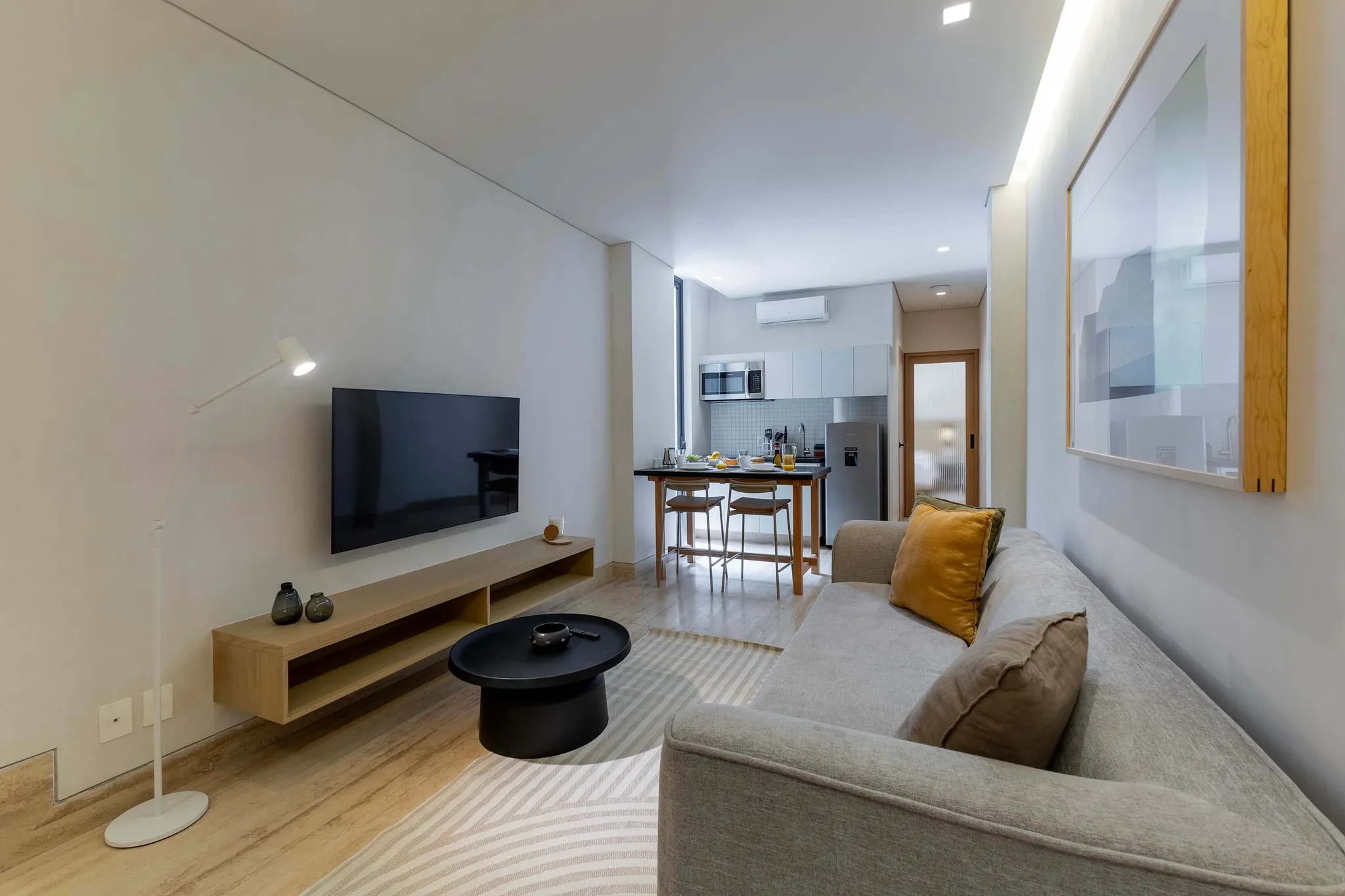 A modern living room and kitchen with a couch, TV, and dining table.