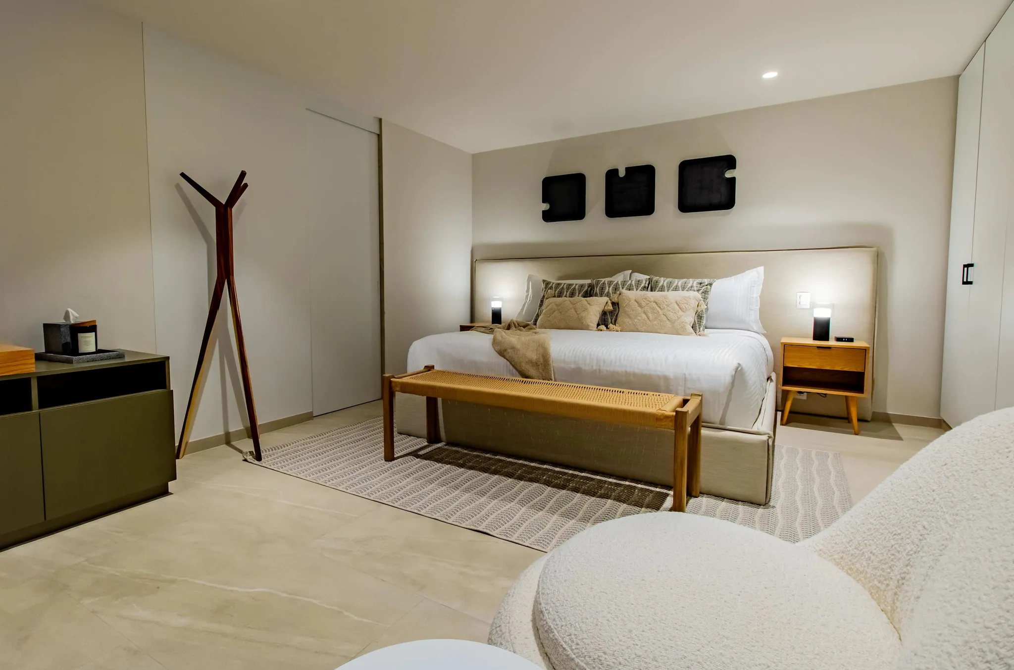 A king-sized bed in a minimalist bedroom with wooden accents and a white boucle armchair.