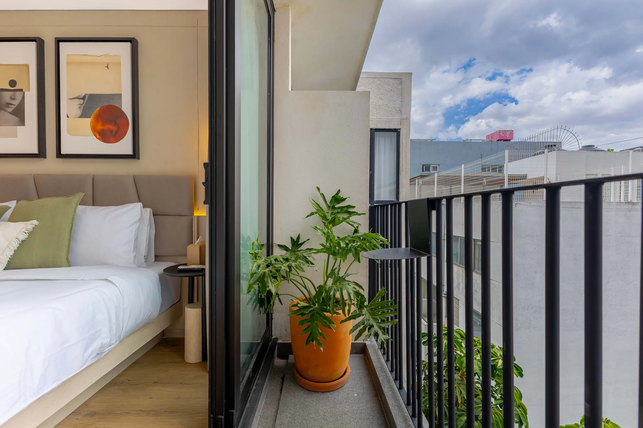Bedroom with a balcony overlooking urban scenery.