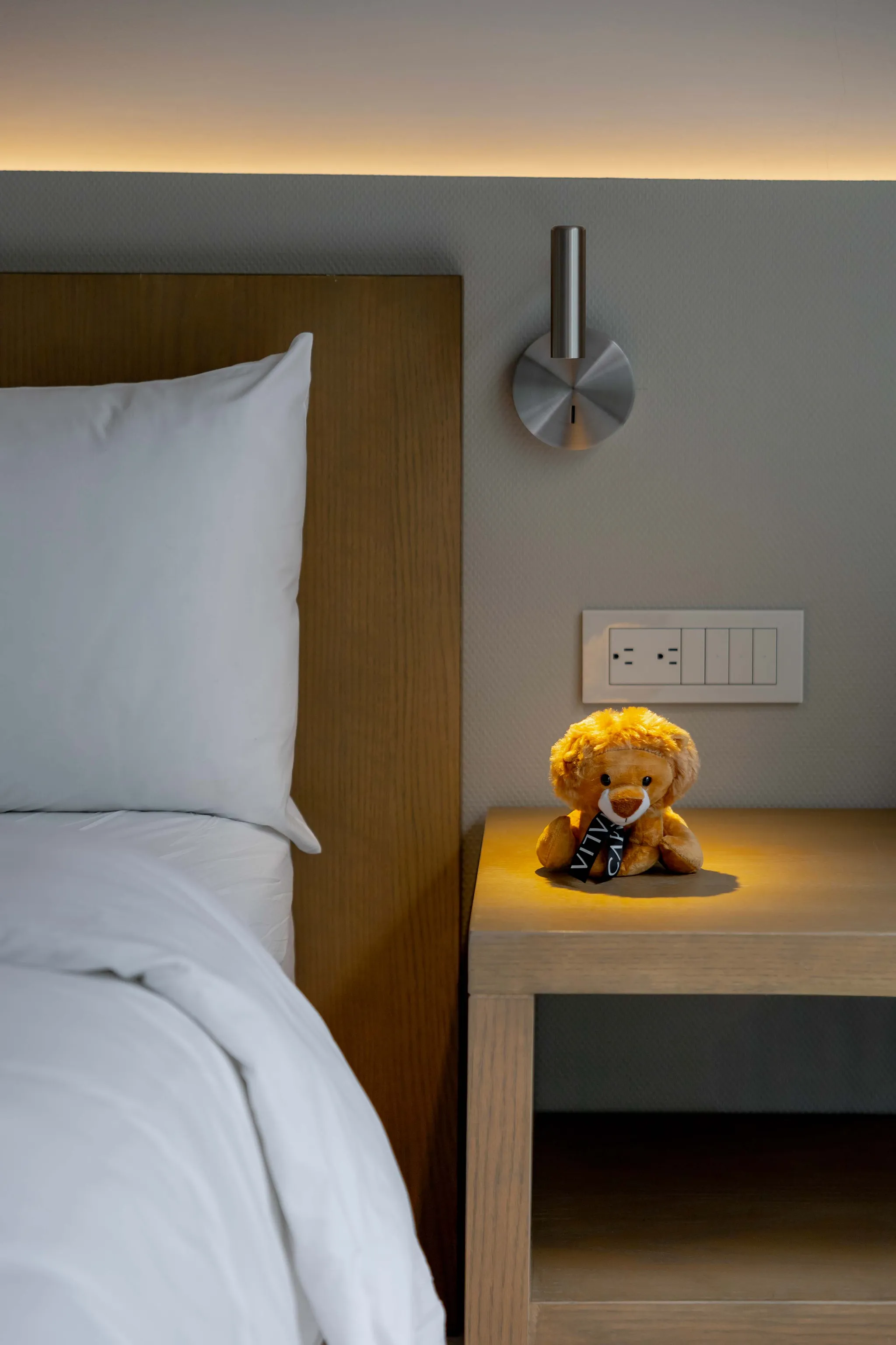 A plush lion toy sits on a wooden nightstand next to a bed.