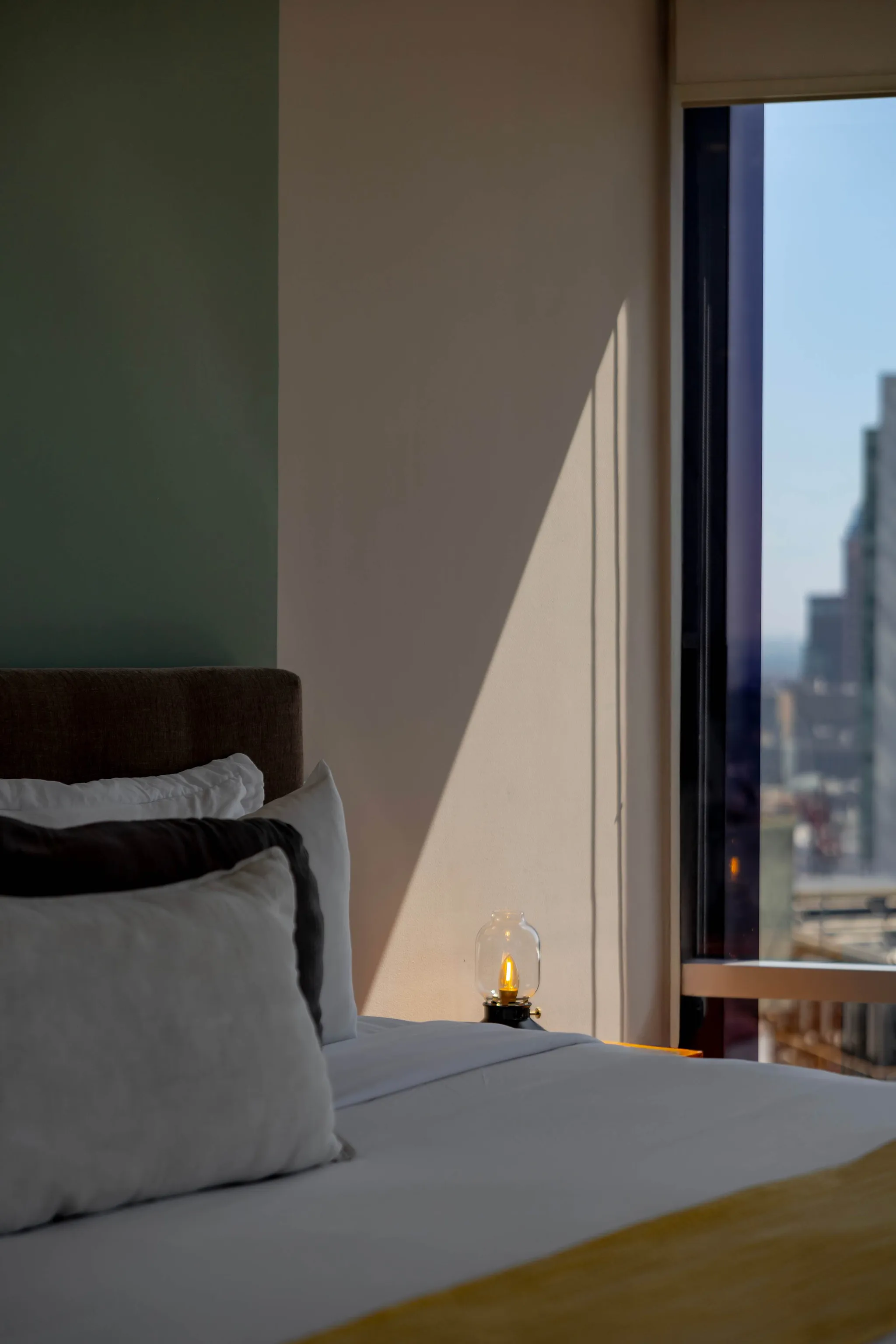 A bedroom with a bed and a window view of a city skyline.