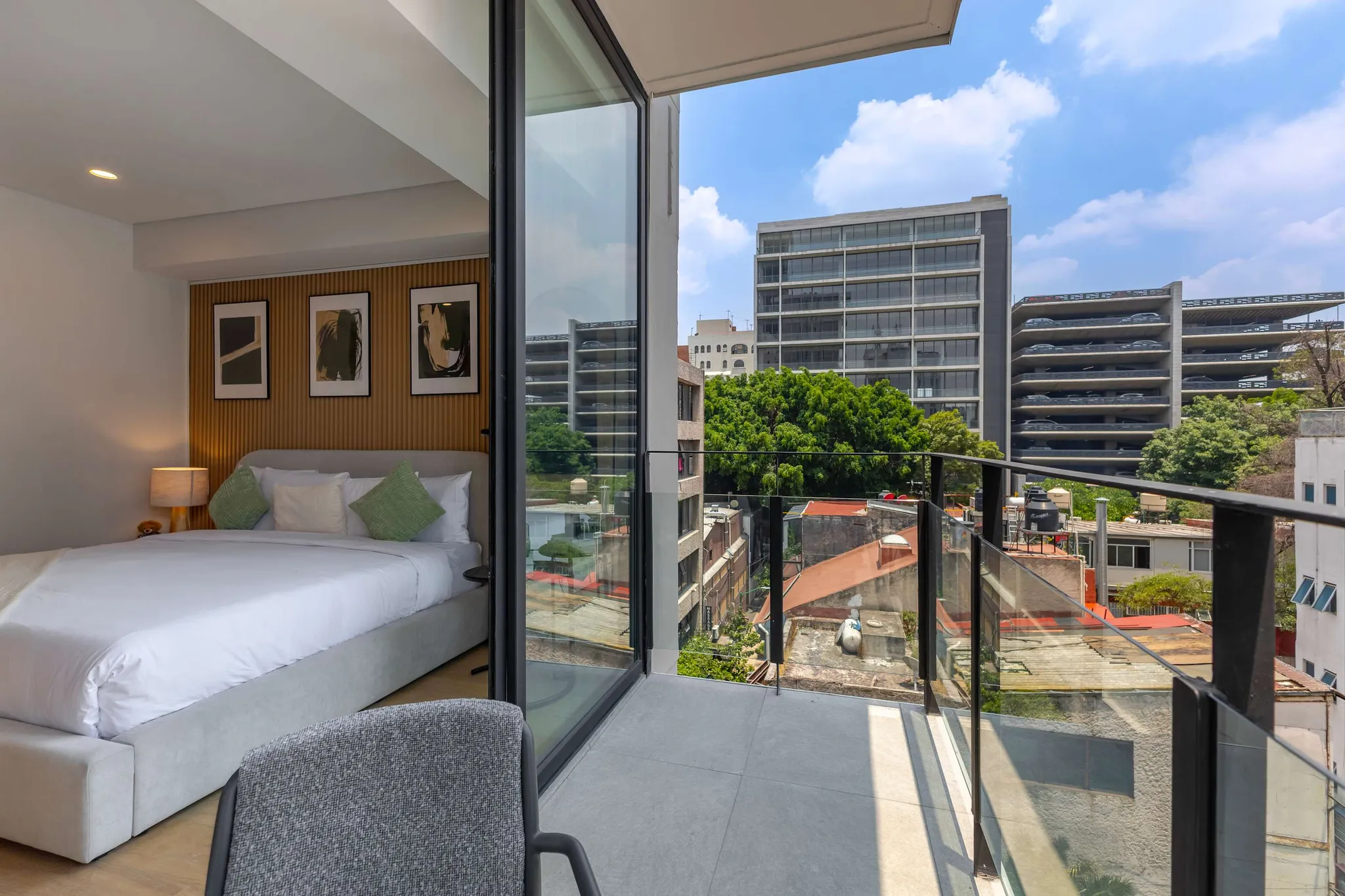 Bedroom with a balcony overlooking city buildings and a parking garage.