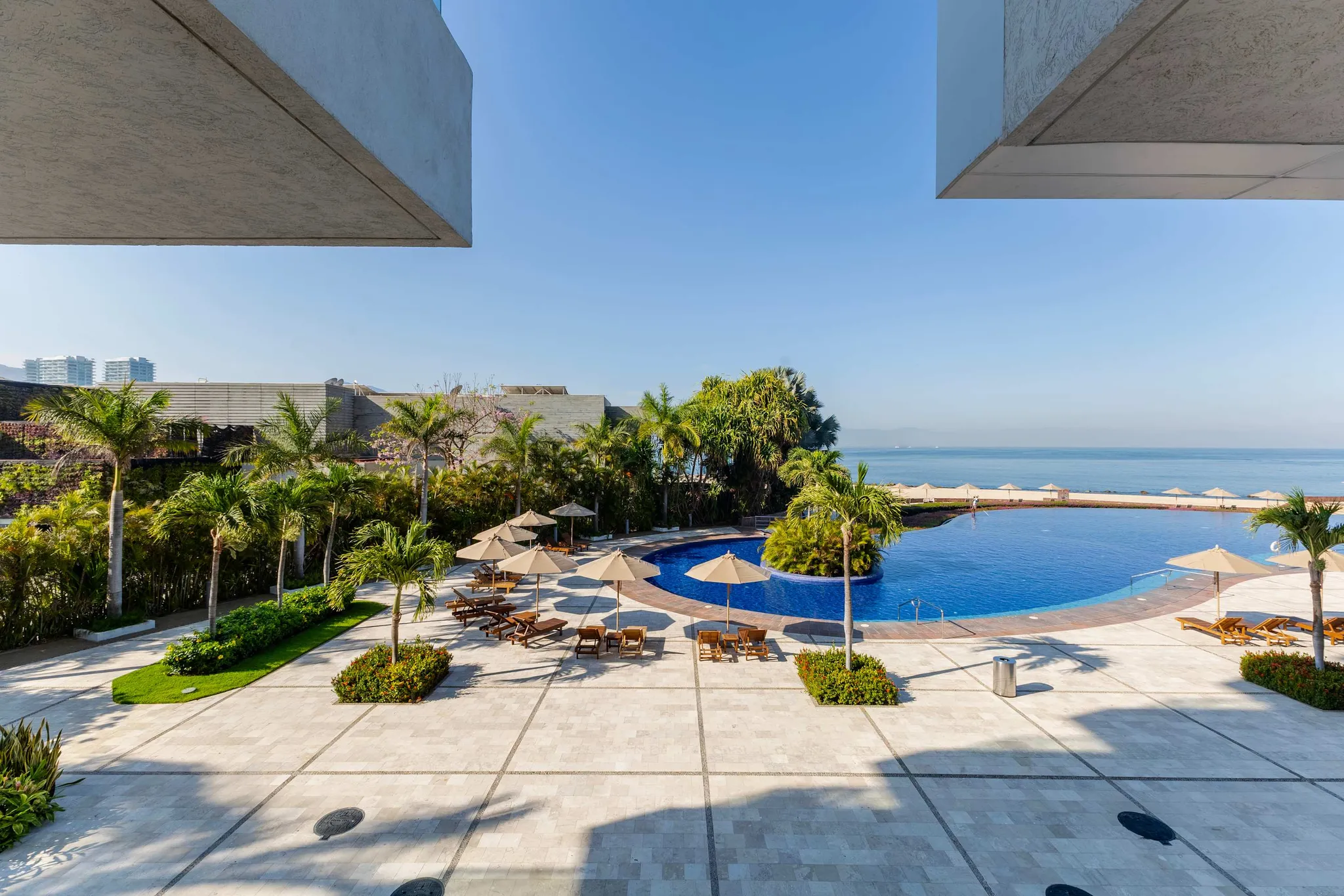 A resort pool with loungers and umbrellas, overlooking the ocean.