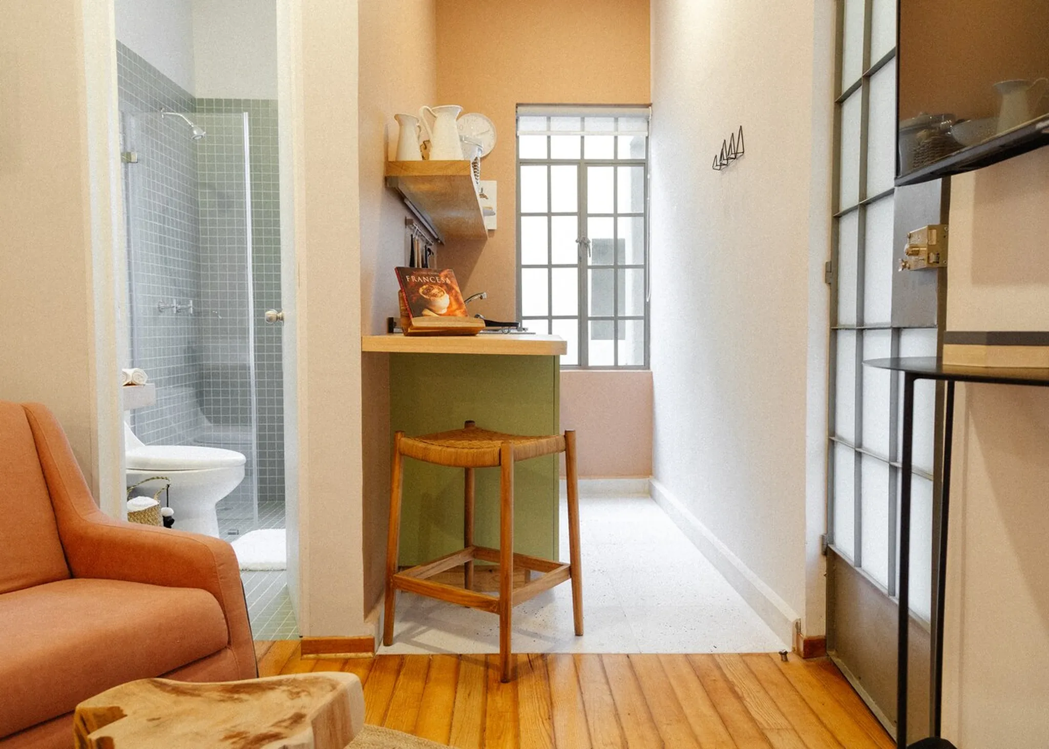 A small room with a toilet, shower, kitchenette, and seating area.
