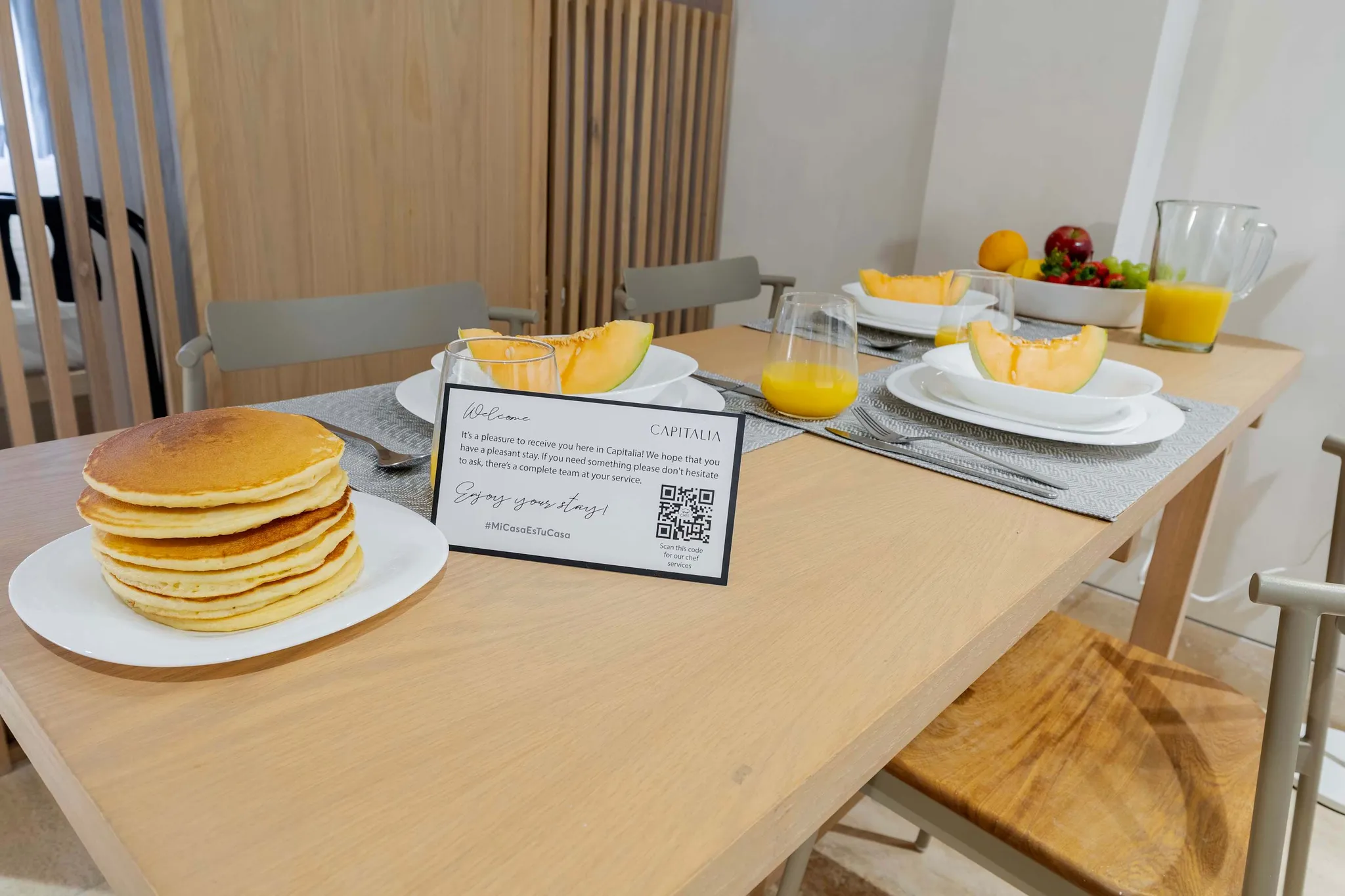 A table set for breakfast with pancakes, fruit, and juice.