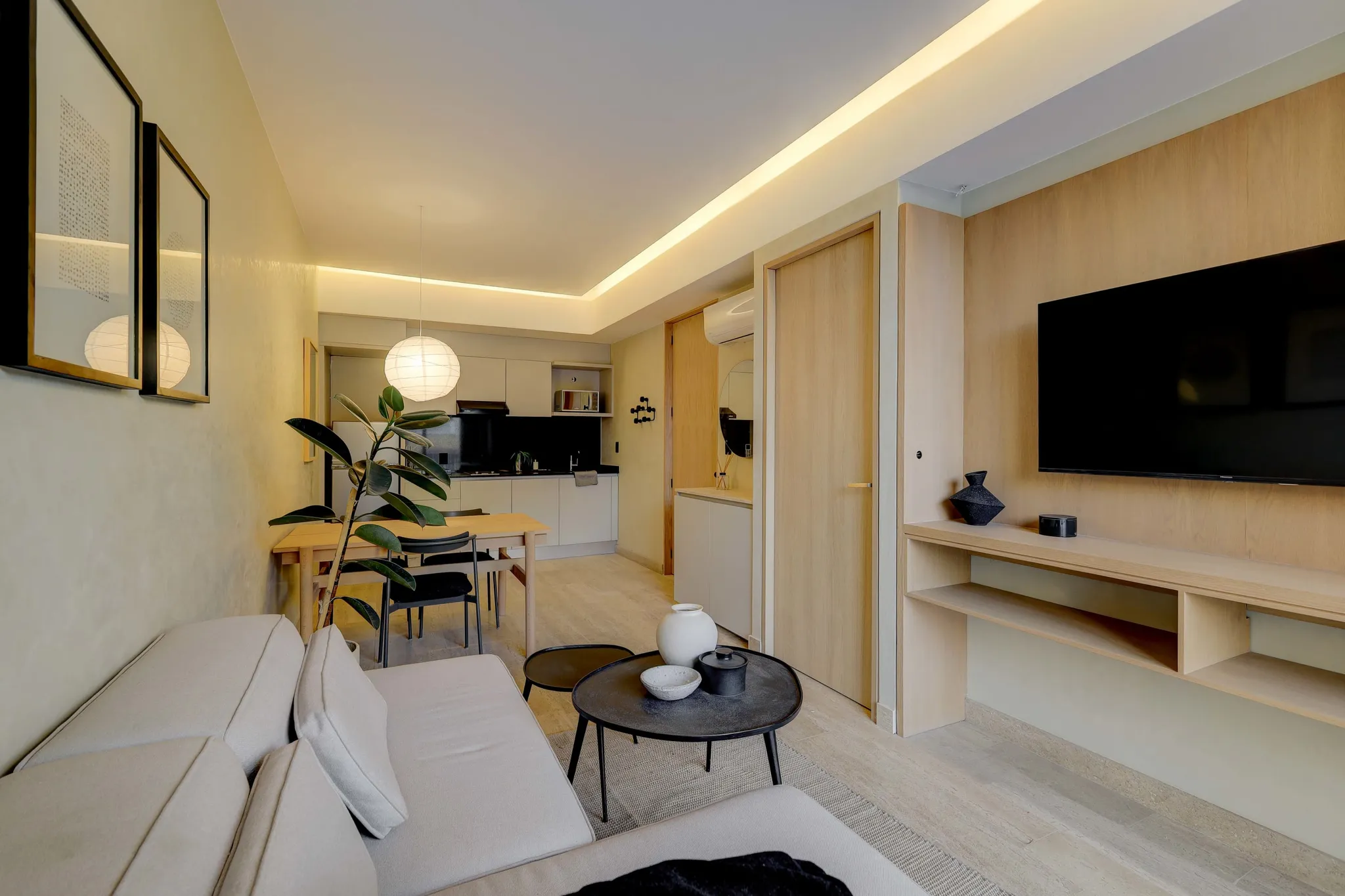 Living room with neutral sofa, coffee table, dining table, kitchen, and mounted tv.