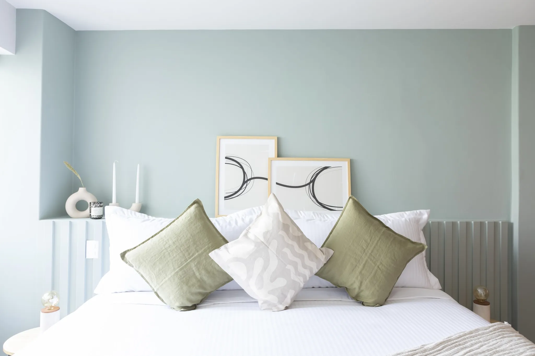 A modern bedroom with a bed, pillows, and framed art.