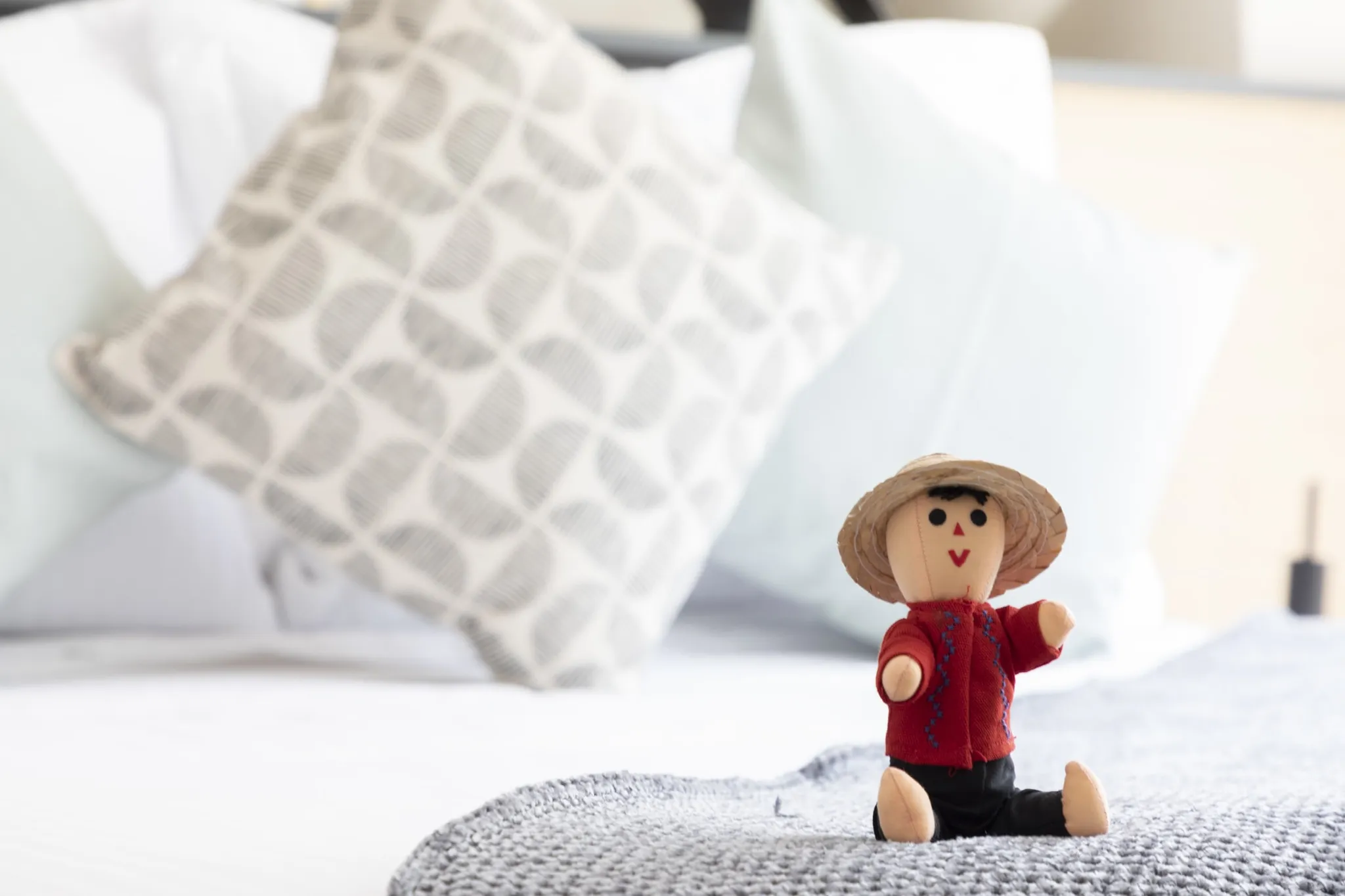 A stuffed doll with a straw hat sits on a bed.