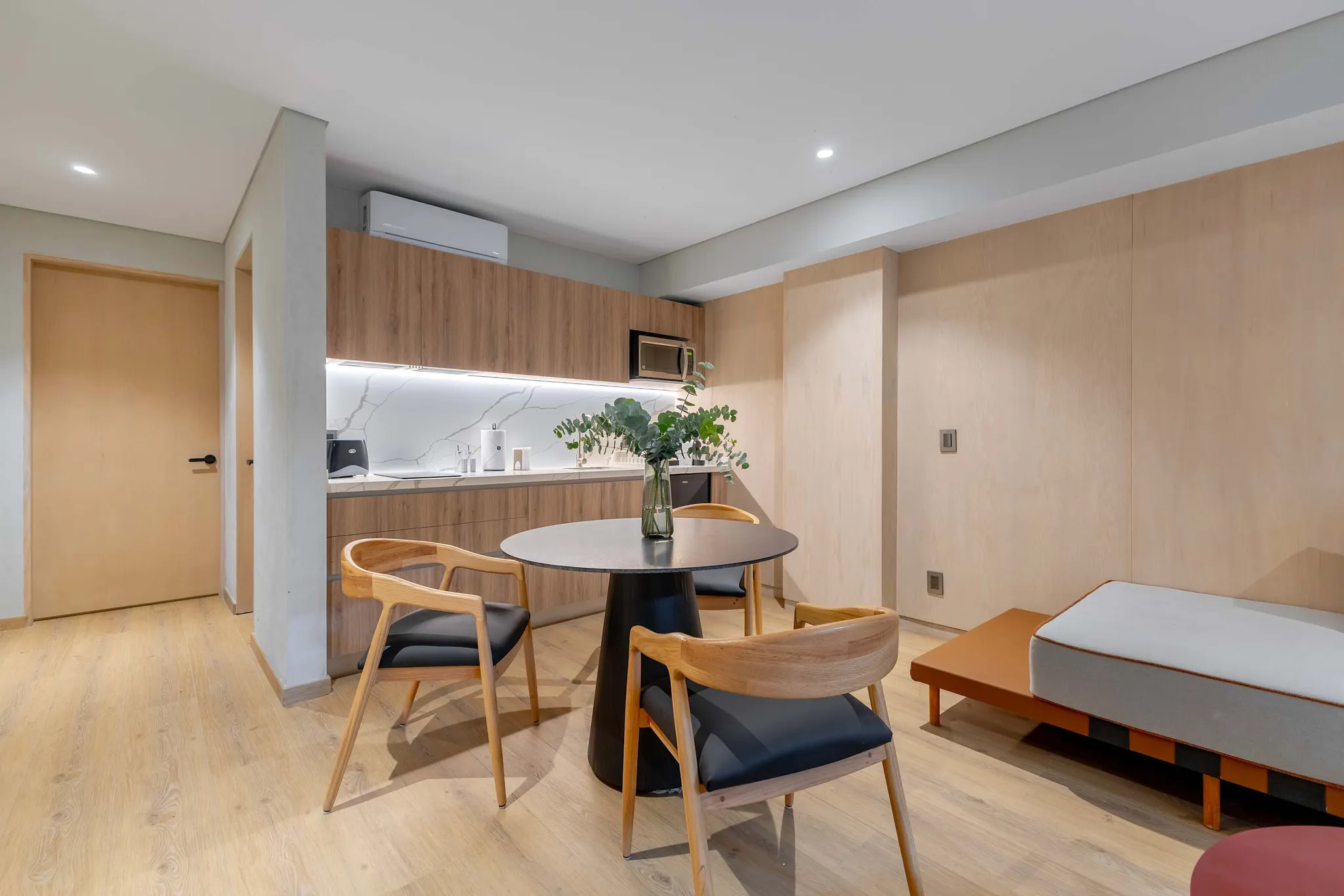 A modern studio apartment with a dining table, chairs, and a small kitchen.