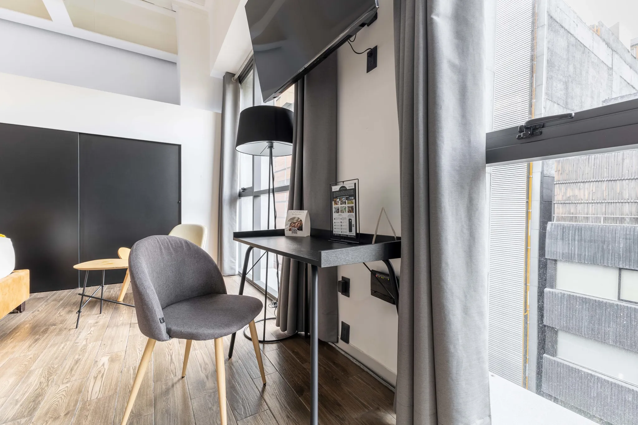 A modern hotel room with a TV, desk, chair, and a large window.