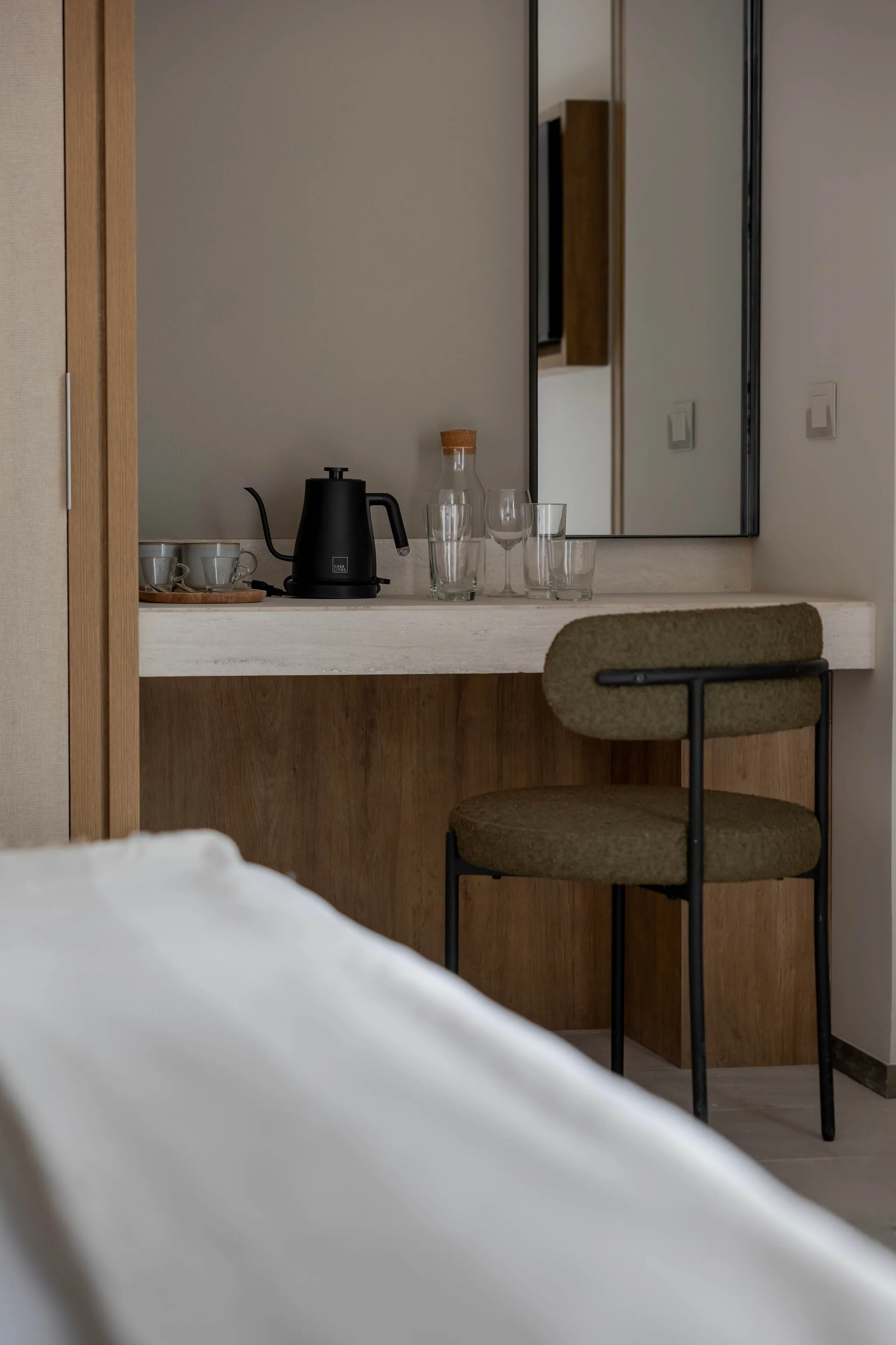 A black electric kettle sits on a shelf next to mugs and glasses.
