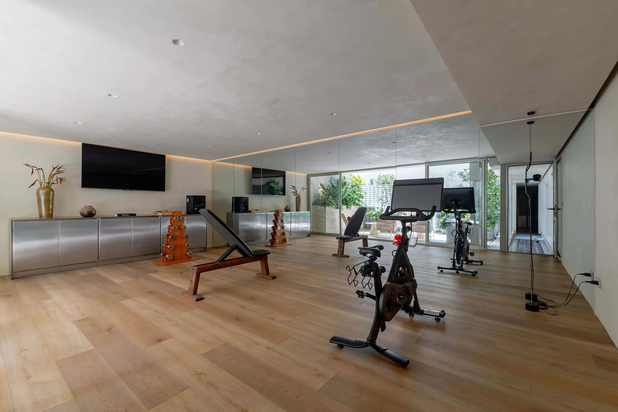Modern home gym with exercise bikes, weight bench, and dumbbells.