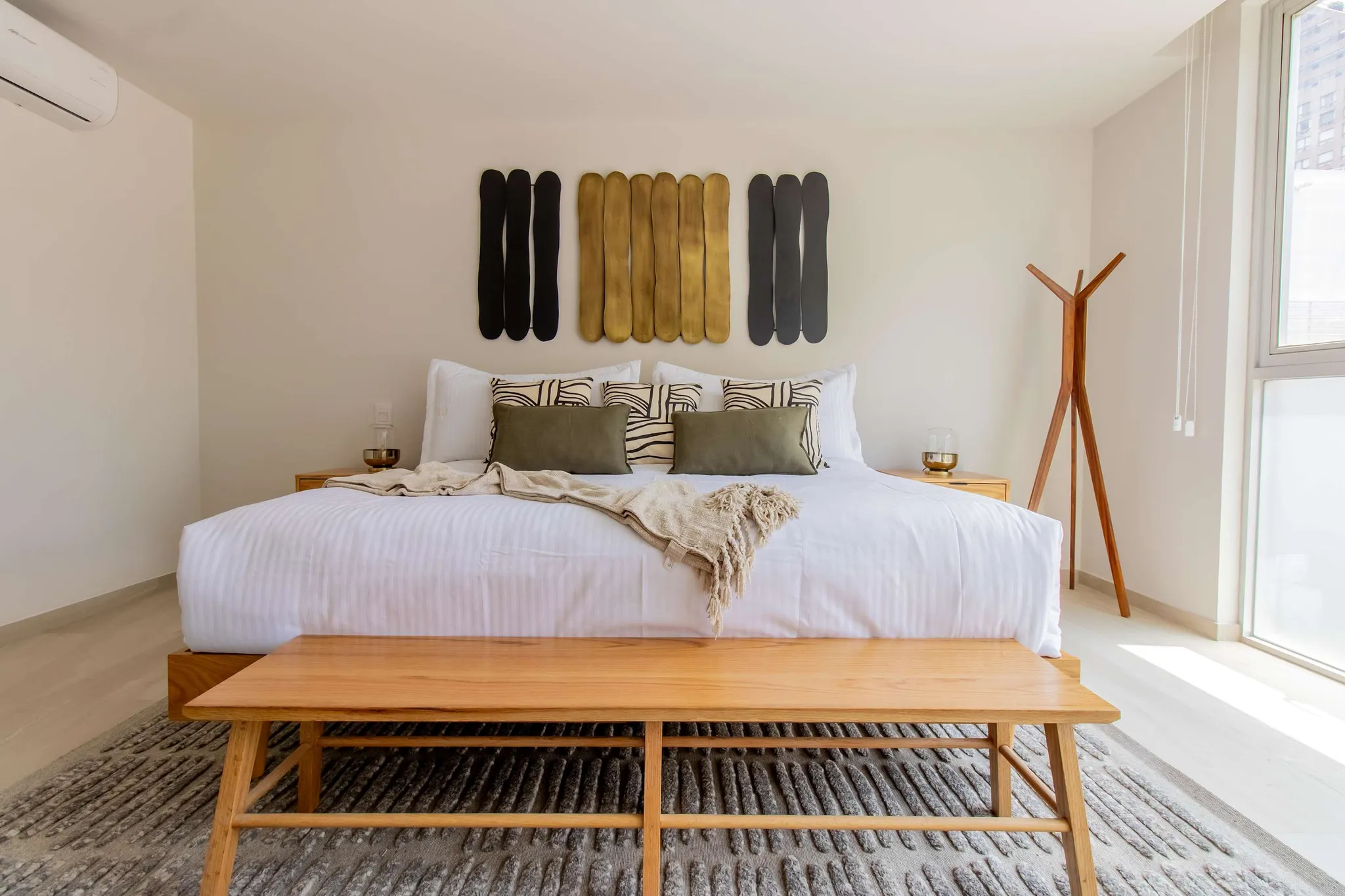 A minimalist bedroom with a large bed, wooden bench, and abstract art.