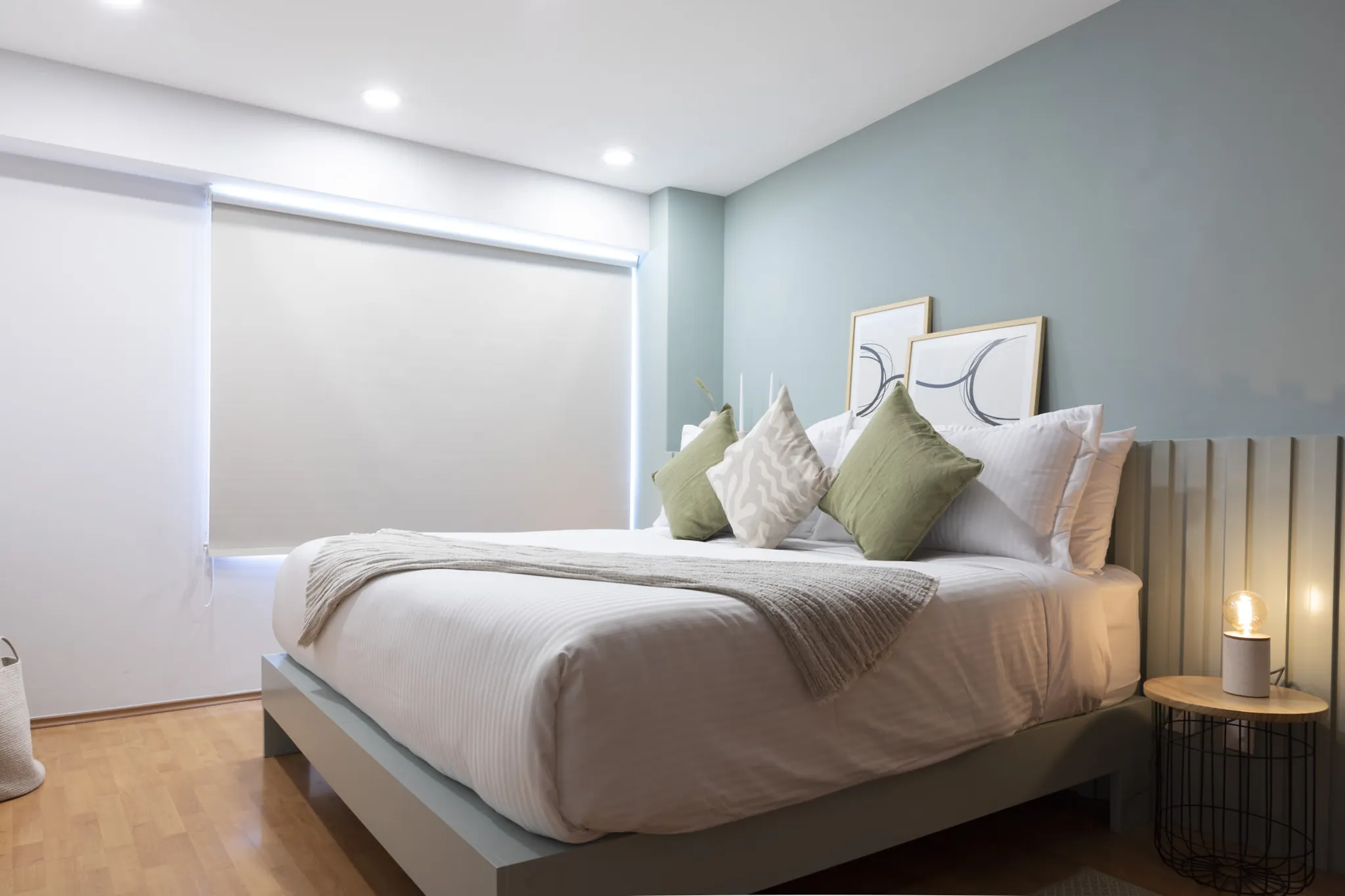 A modern bedroom with a light blue accent wall, a large bed with white linens and decorative pillows