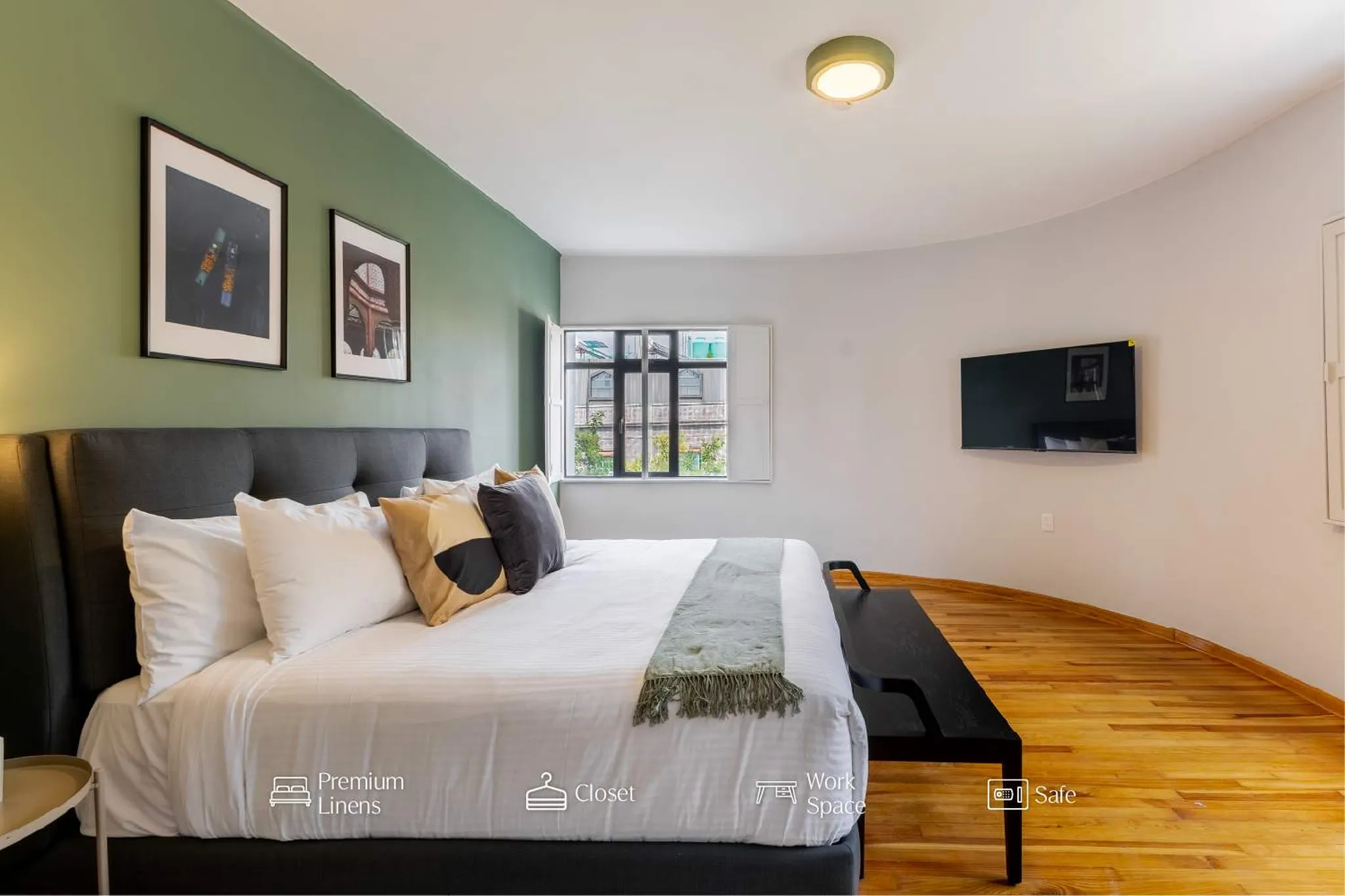 A large bed with white linens, pillows, and a green throw is in a bedroom with green and white walls