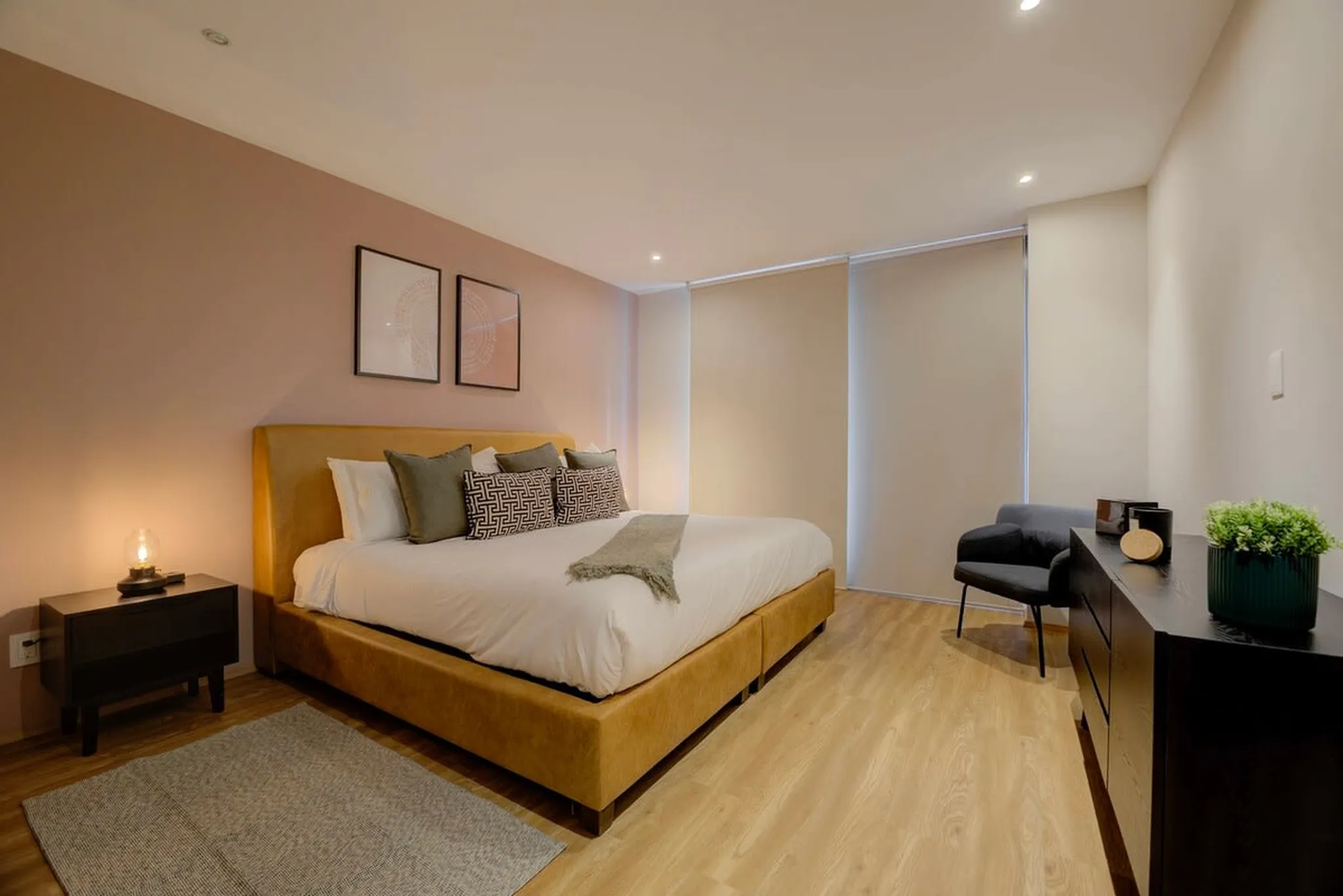 A modern bedroom features a bed with a gold headboard, two framed pictures, and a bedside table.