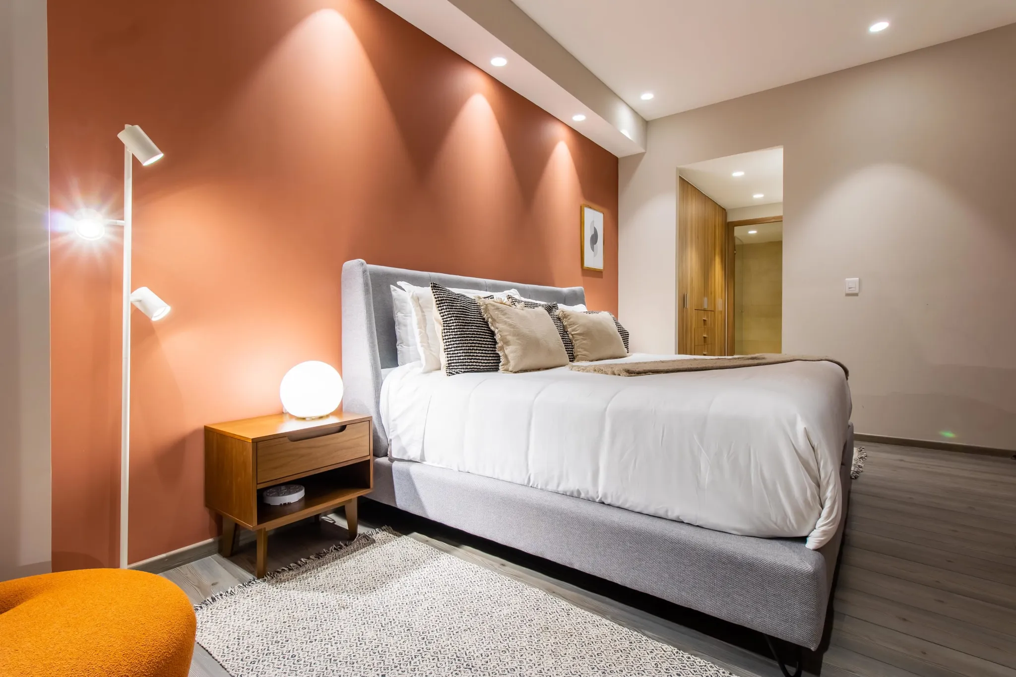 A cozy bedroom with an orange accent wall, a king-size bed, and modern lighting.
