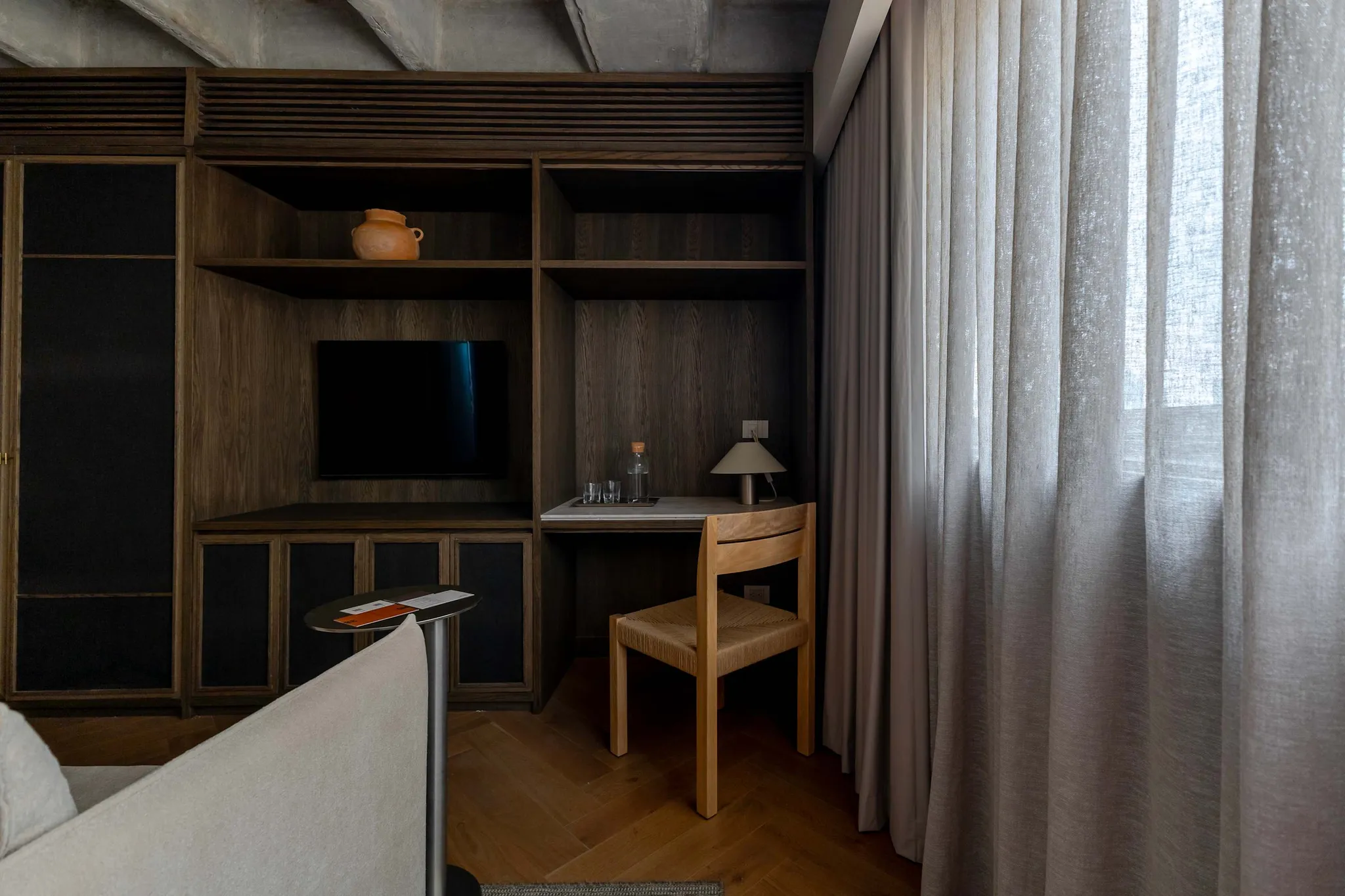 A dark wood built-in entertainment center with shelves, a TV, and a desk, next to a window with ligh