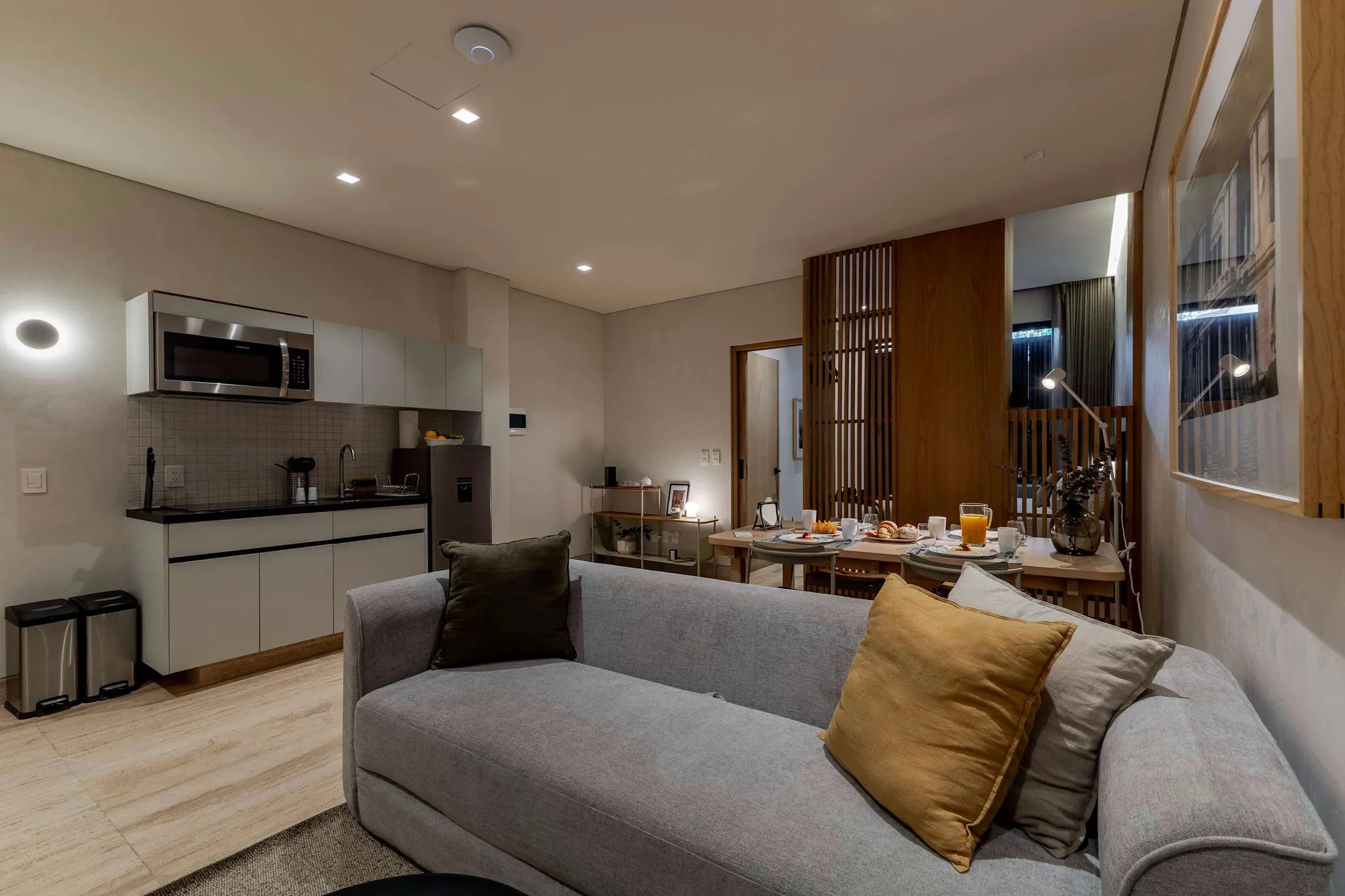 Open living and dining space at Casa Calderon with a grey sofa, warm wood slat partition, and a breakfast table set for two.