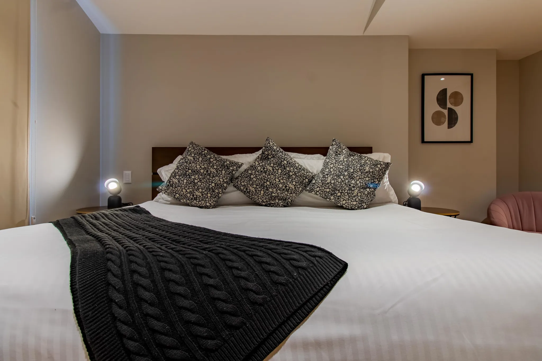 A bed with a dark gray cable-knit throw blanket and patterned pillows.