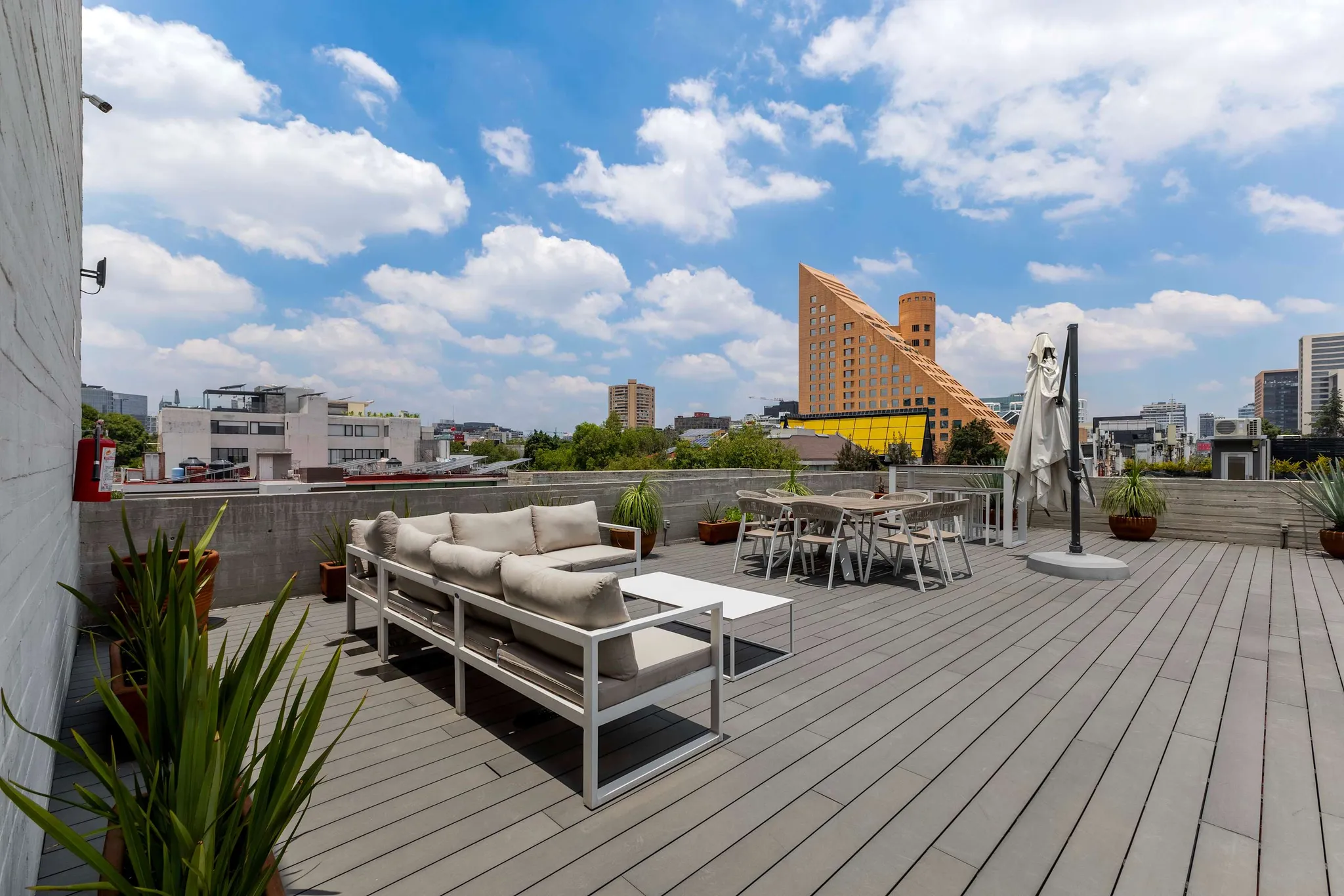 A rooftop patio with lounge seating, a dining set, and a city view under a blue sky.