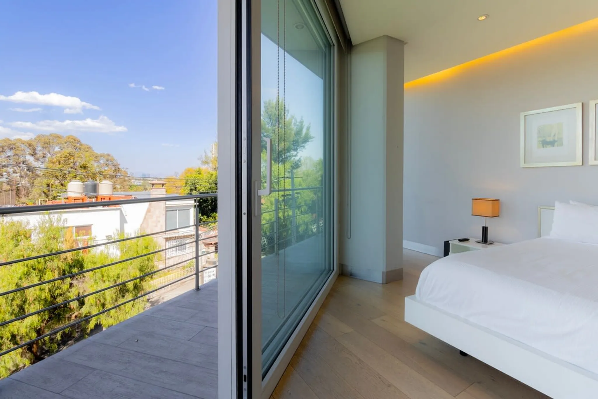 A bedroom with a large sliding glass door opening onto a balcony, showcasing a bed and a nightstand.