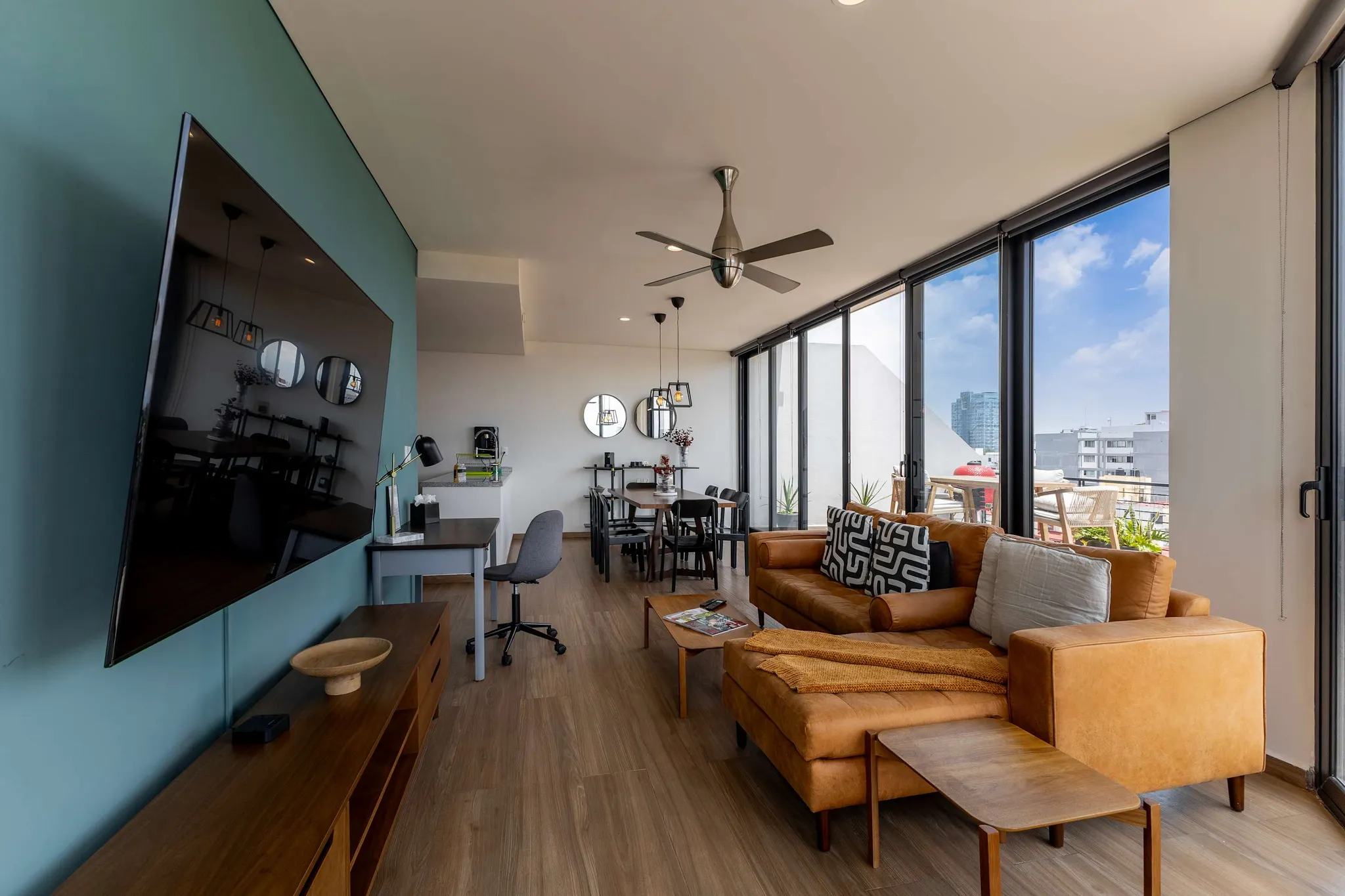 Bright living and dining area with a leather sofa, wooden floors and a workspace corner at Downtown del Valle.