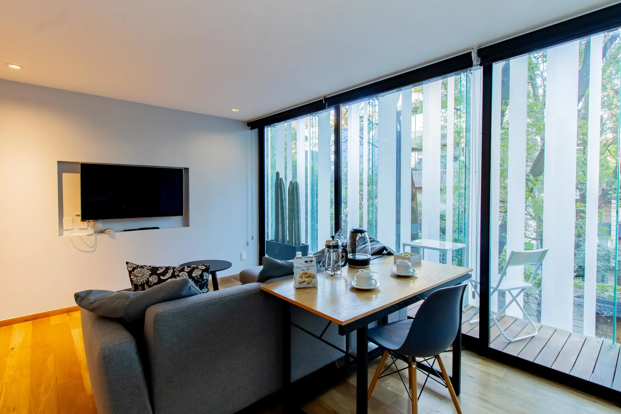 Modern living room with a gray sofa, dining table, and a large window with vertical blinds.