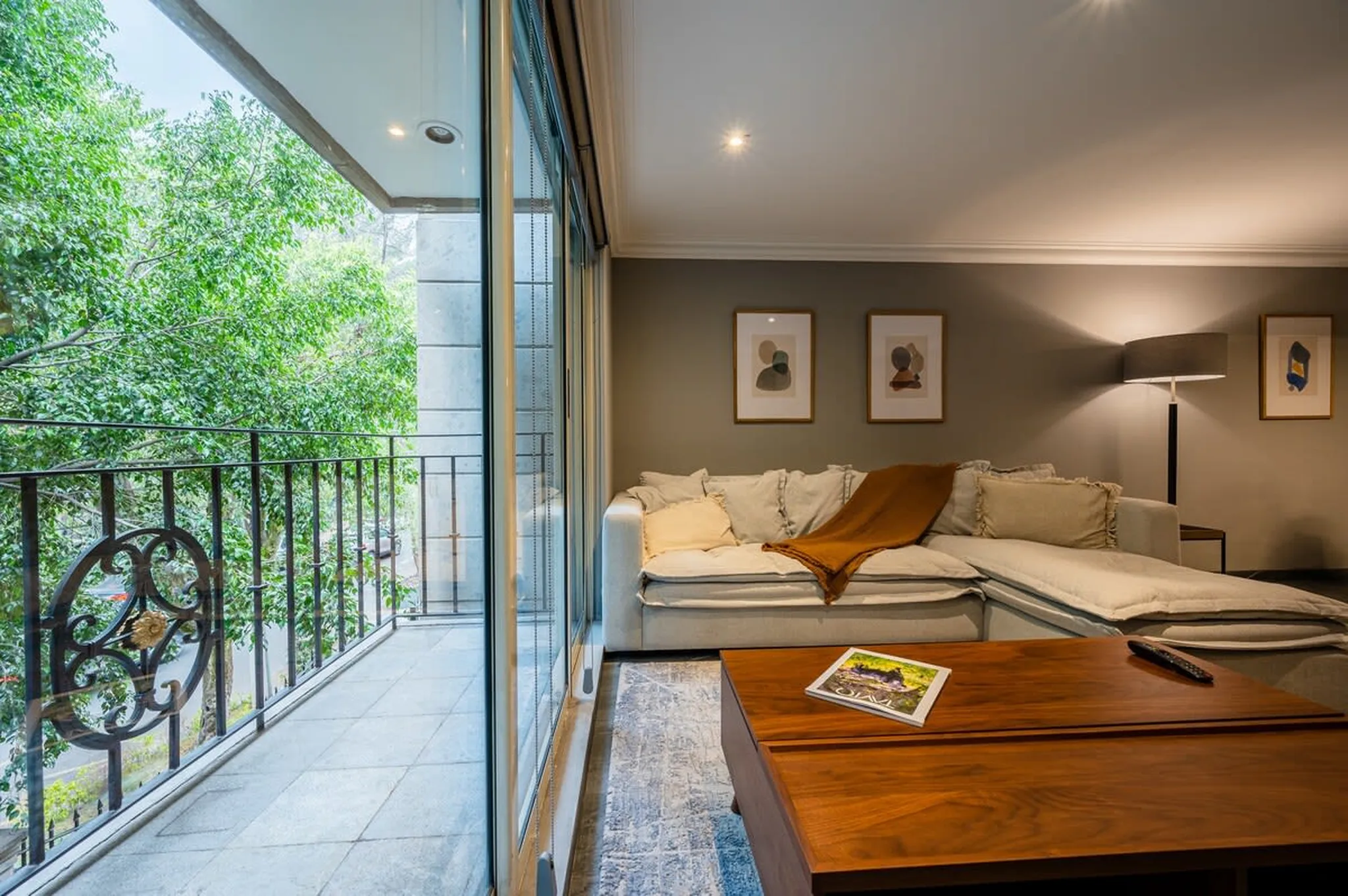 A contemporary living room with a balcony overlooking lush greenery, featuring a sectional sofa and