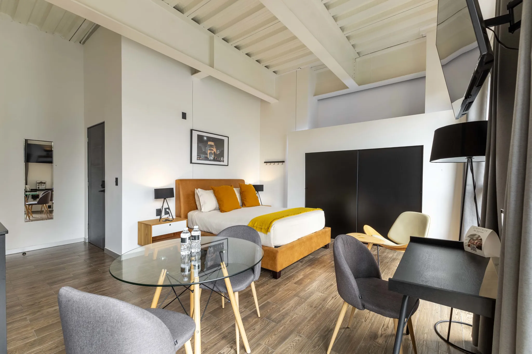 A modern bedroom with a bed, seating area, and a desk.