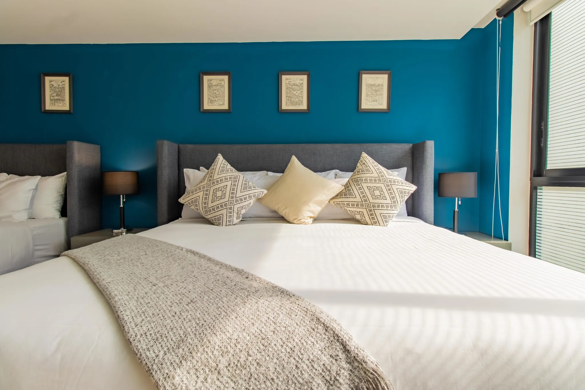 A bedroom with a large bed, blue walls, and framed artwork.