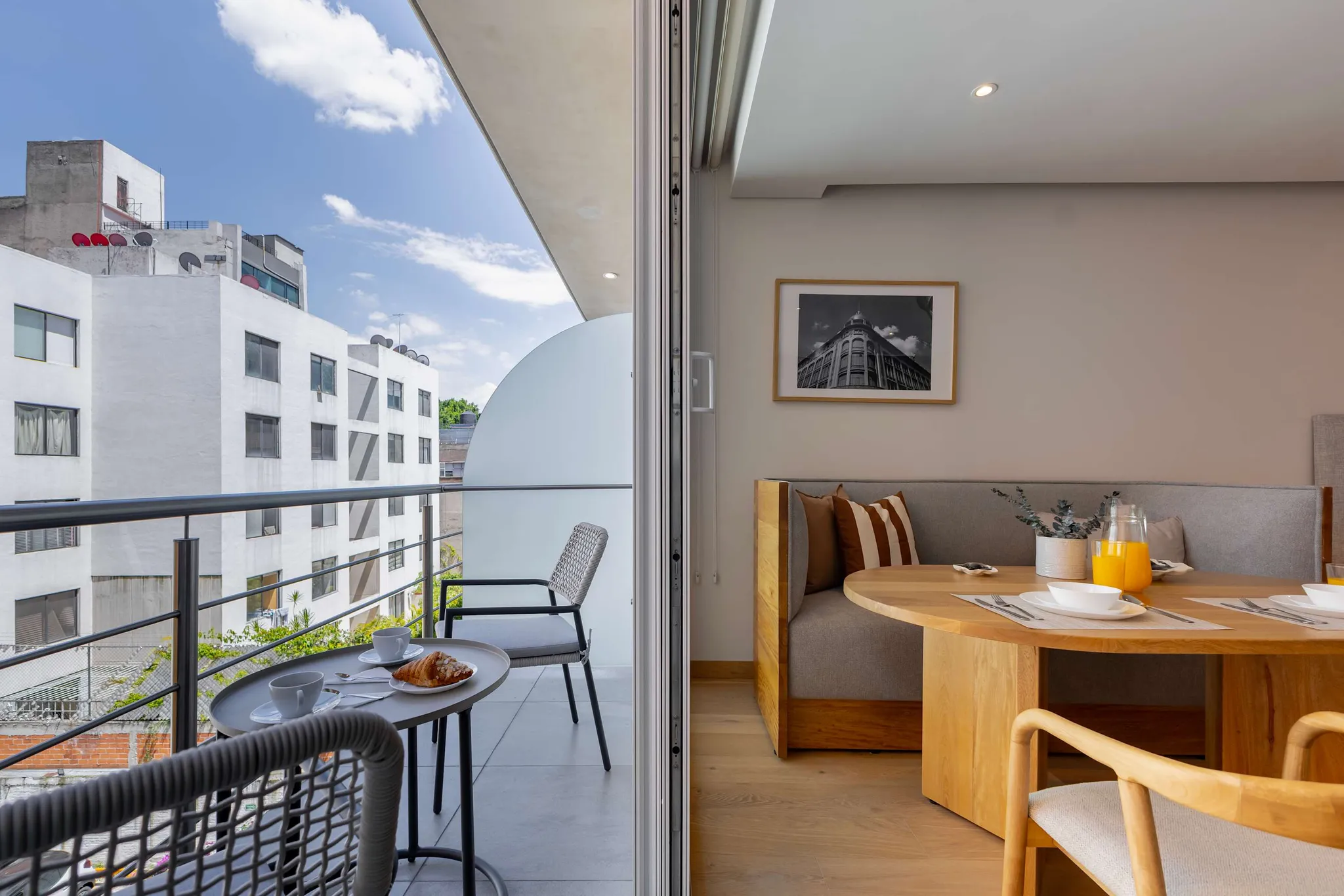 A balcony with chairs and a table, and an interior with a dining table and bench.