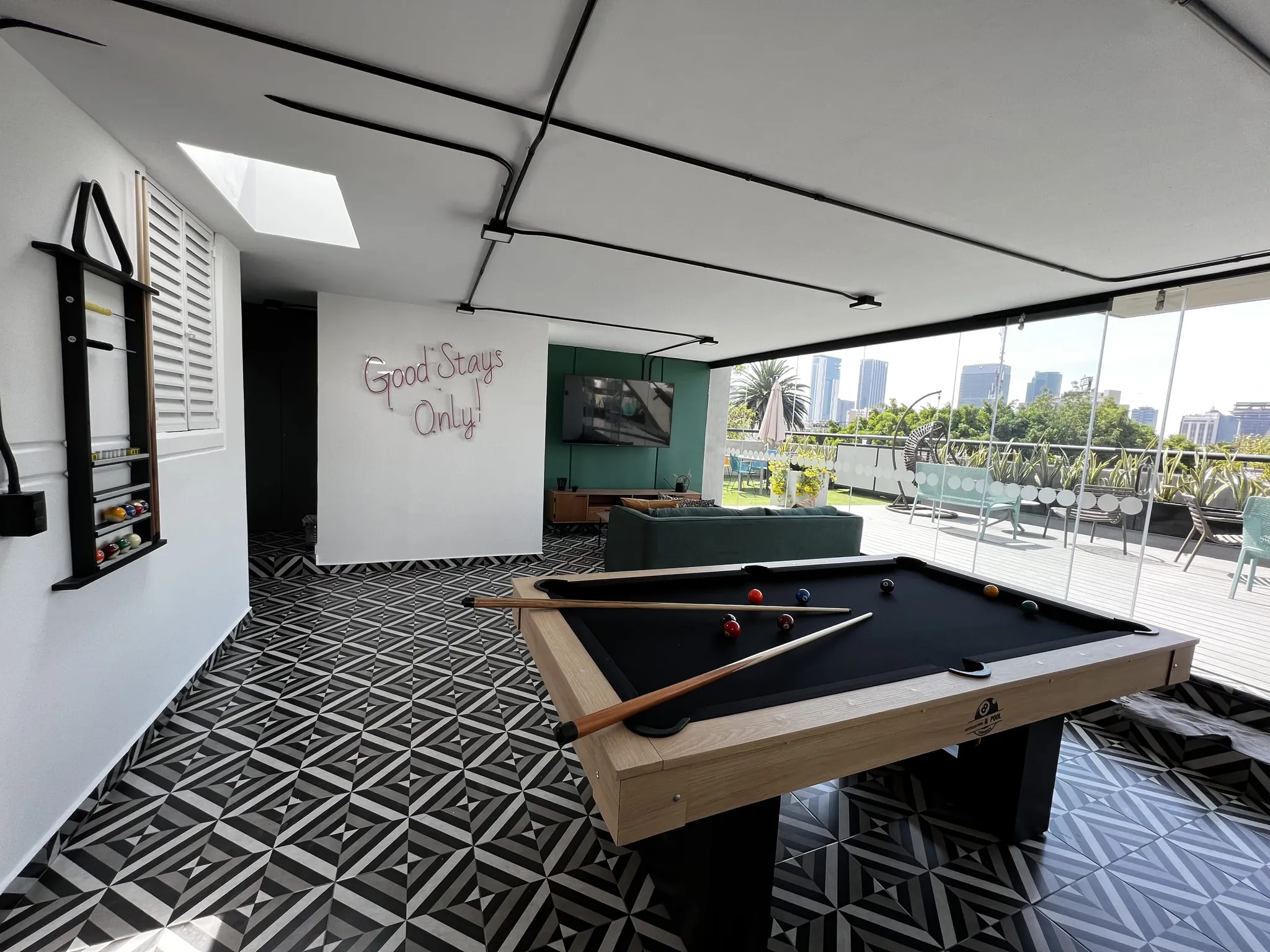 A pool table and sofa are in a room with a modern design, featuring patterned floors and a city view