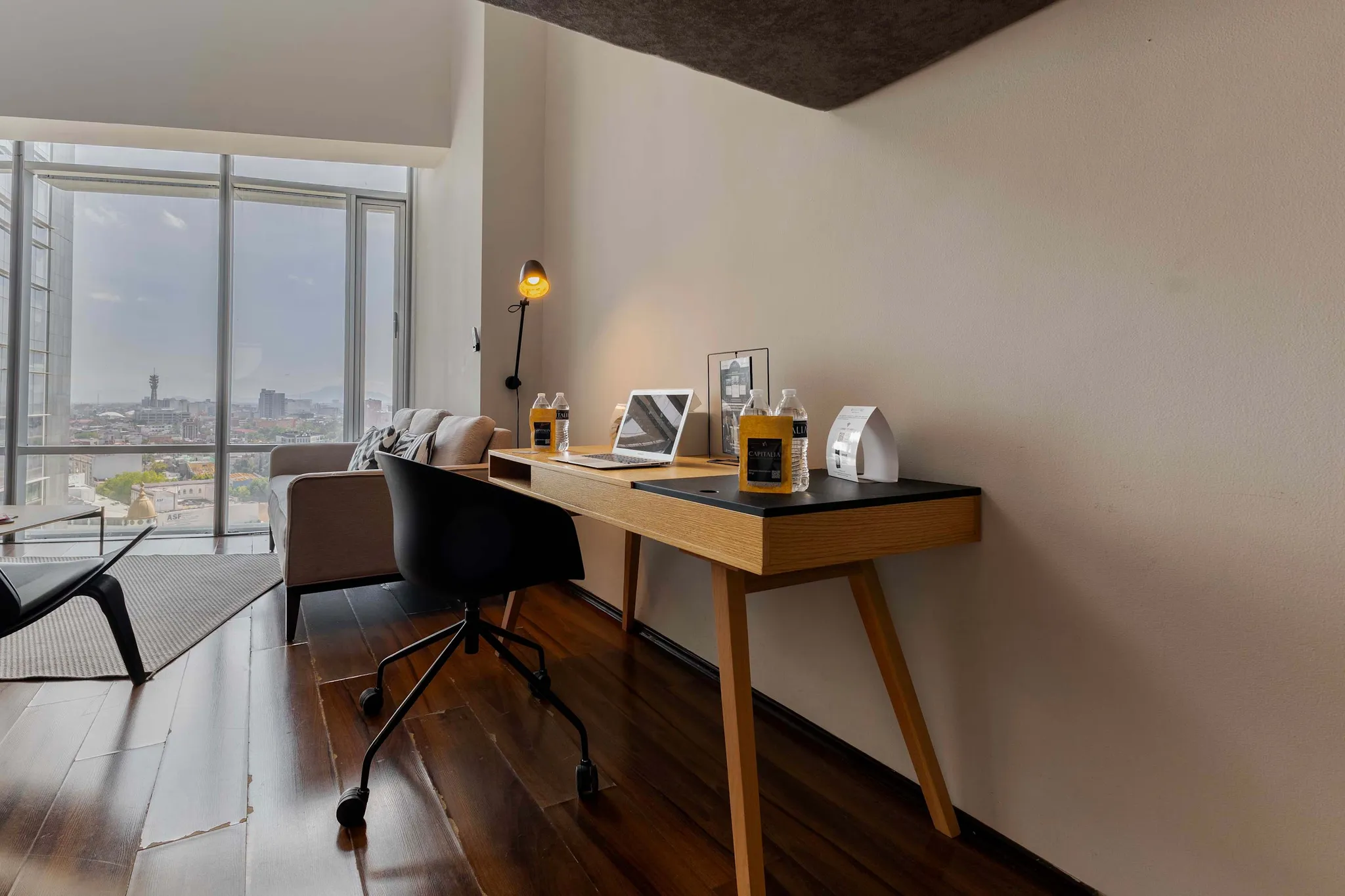 A desk with a laptop and water bottles in front of a window overlooking a city.