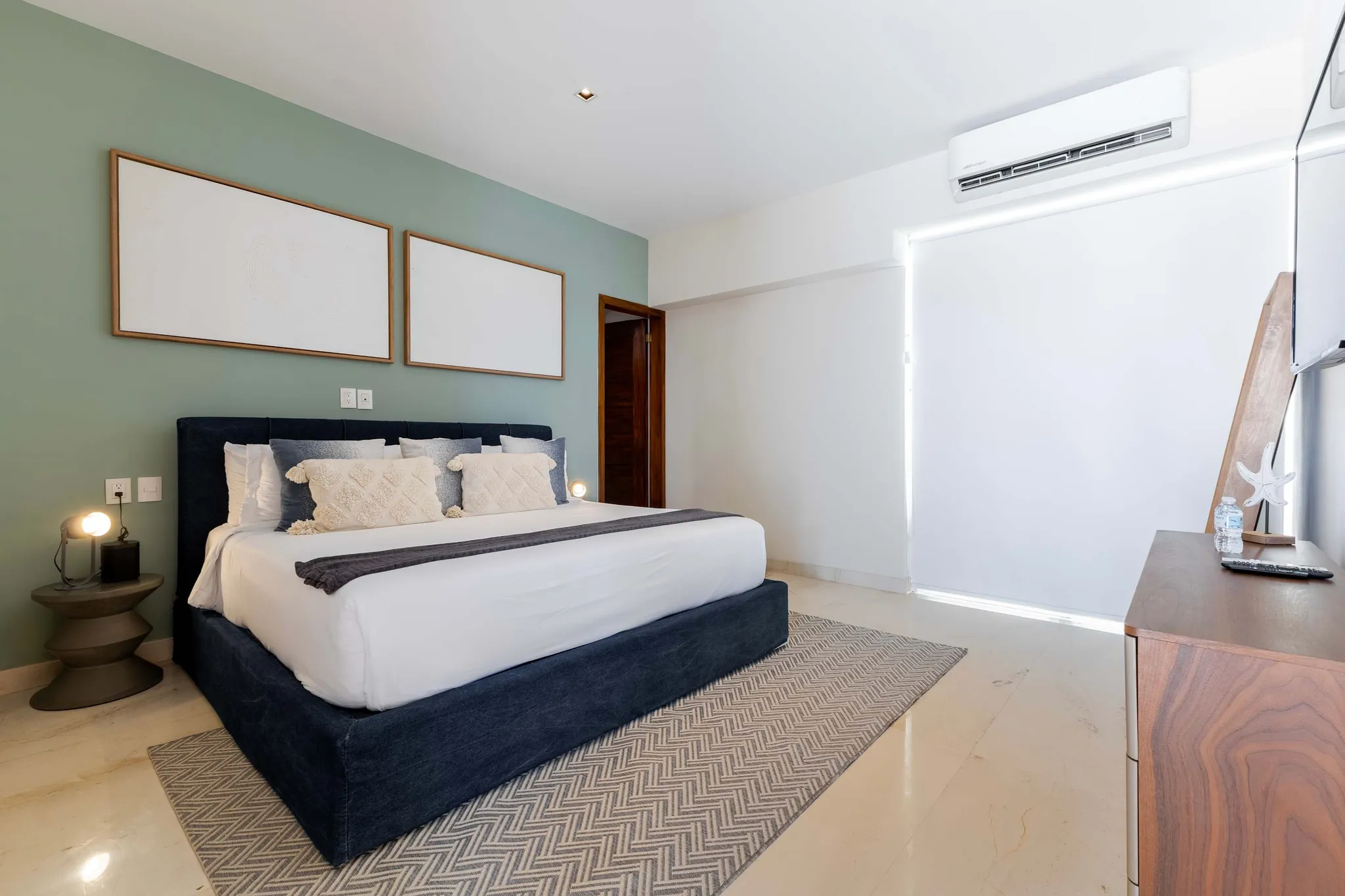 A modern bedroom with a king-size bed, a green accent wall, and a wooden dresser.