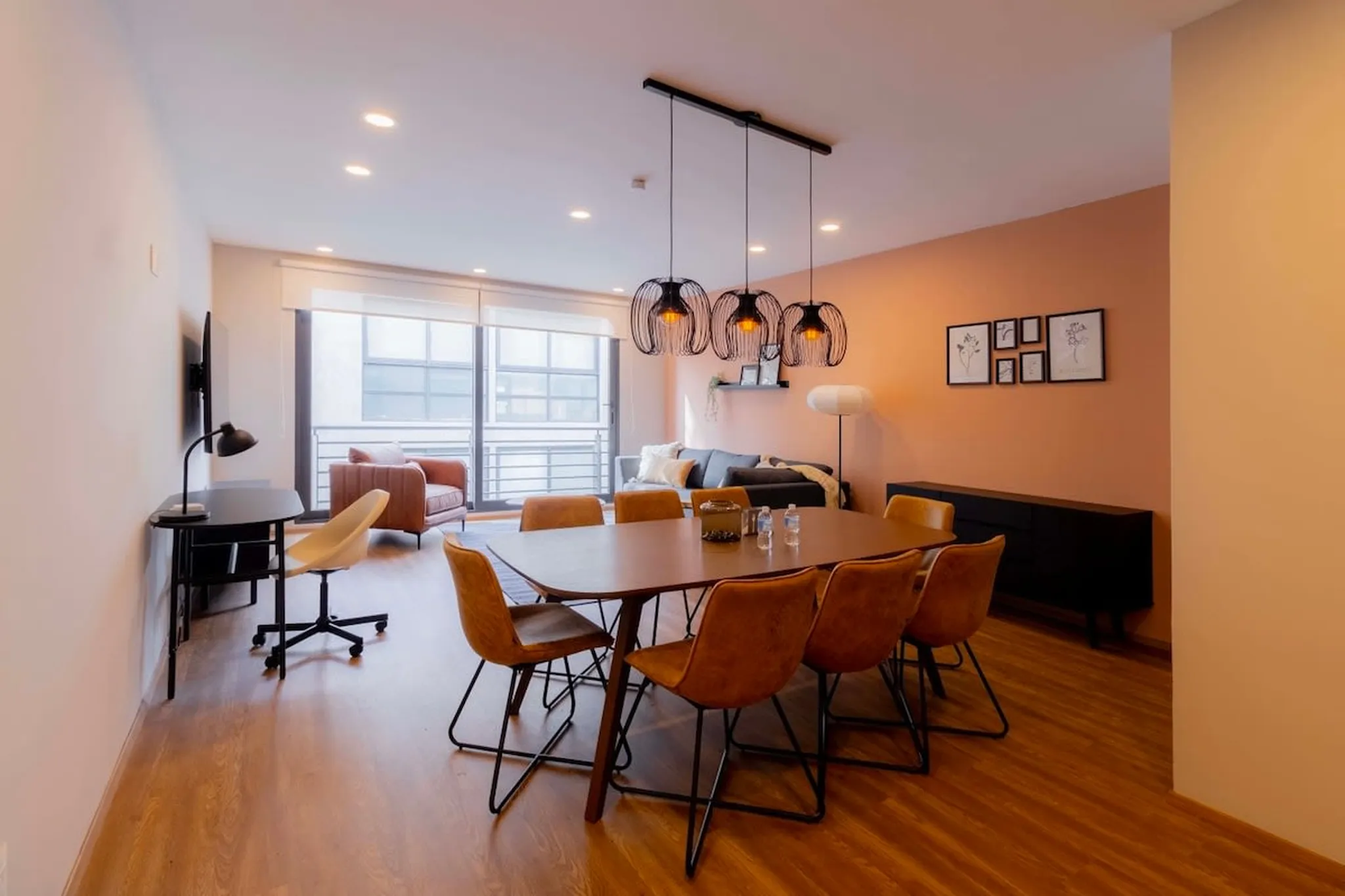 A dining room with a wooden table and brown chairs, a sofa, and a desk with a chair.