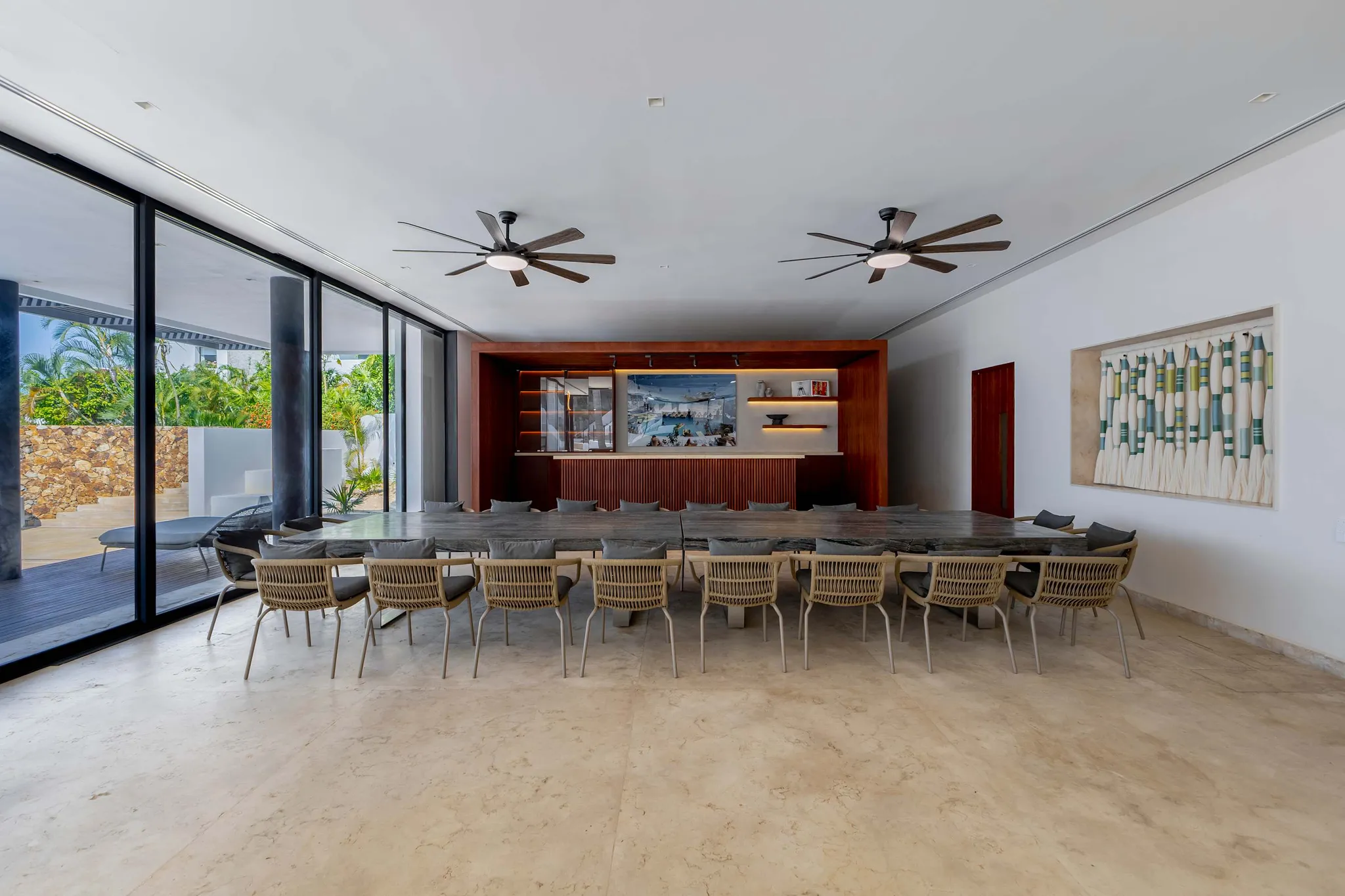 A modern dining room with a long wooden table and chairs, a bar area, and ceiling fans.