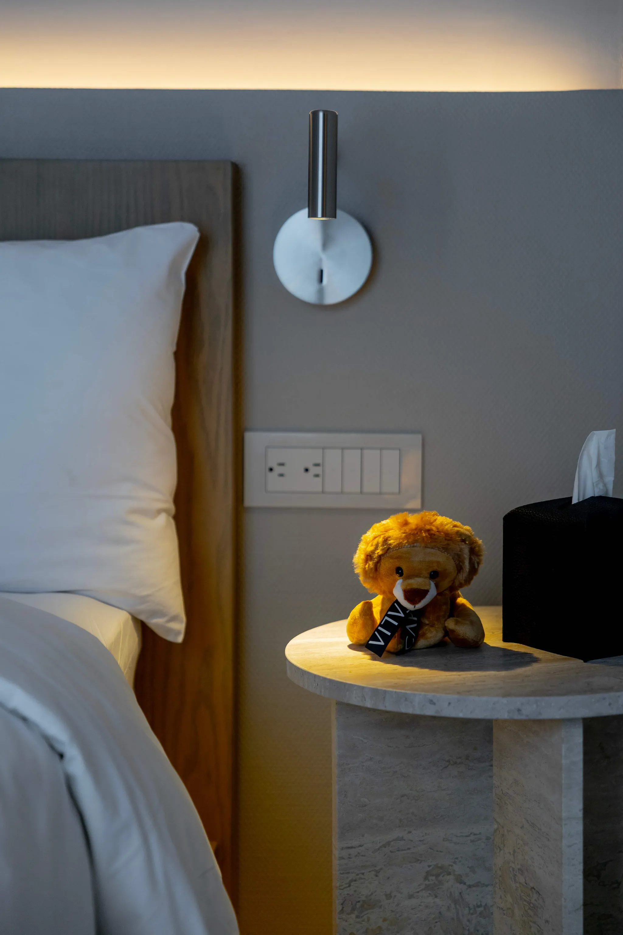 A stuffed lion sits on a bedside table next to a tissue box.