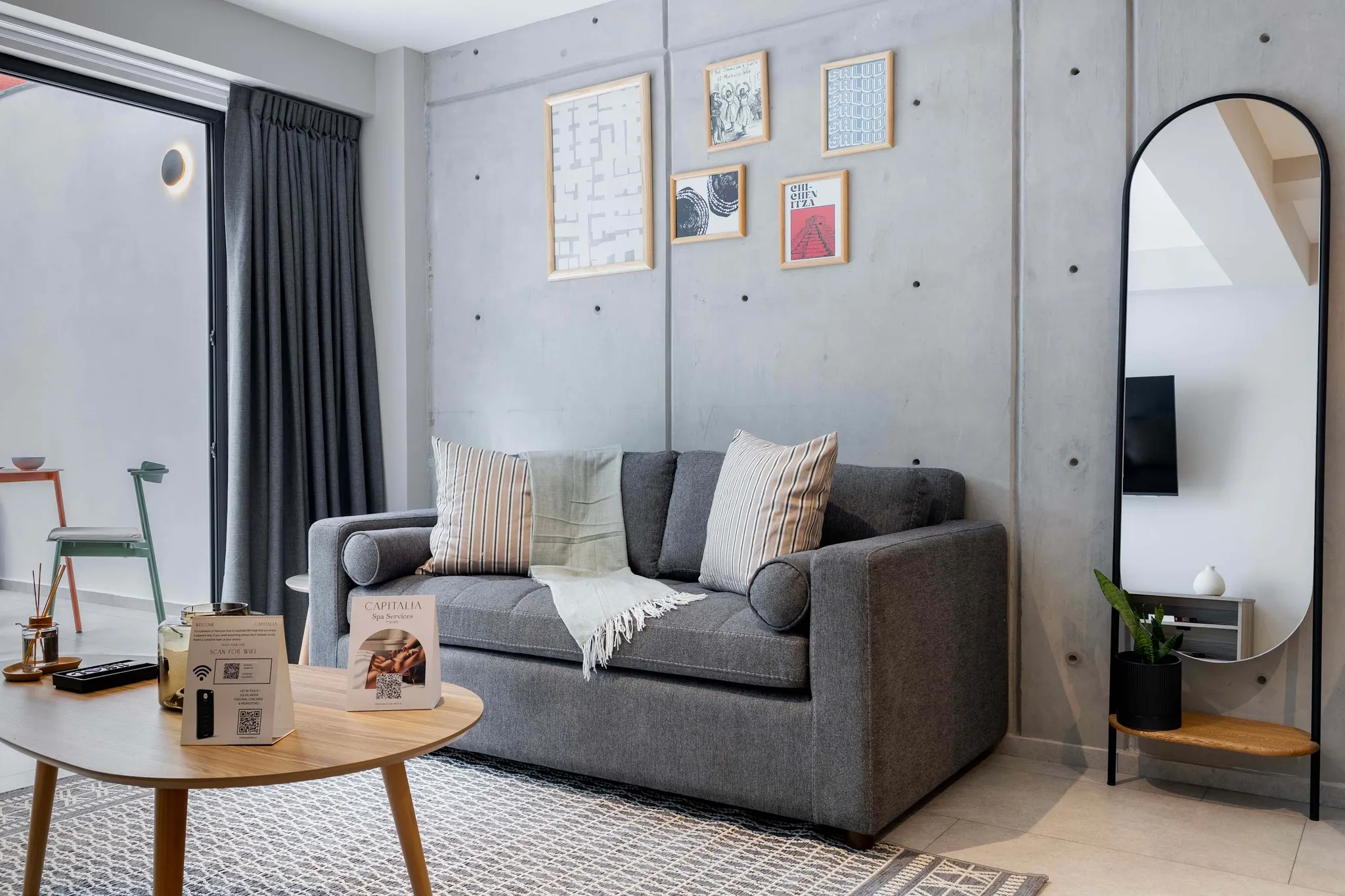 A modern living room with a grey couch, wooden table, and framed art on a concrete wall.