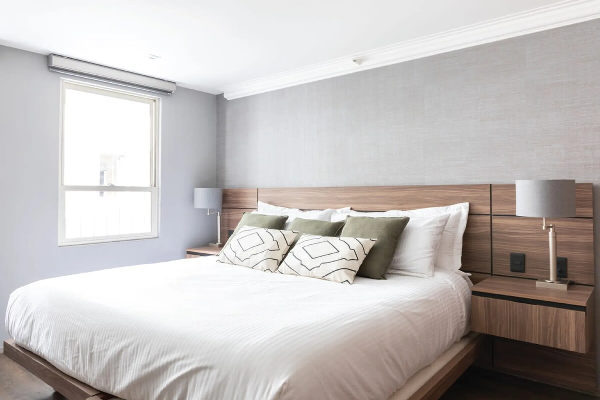 A hotel bedroom with a king-size bed, grey walls, and a window.