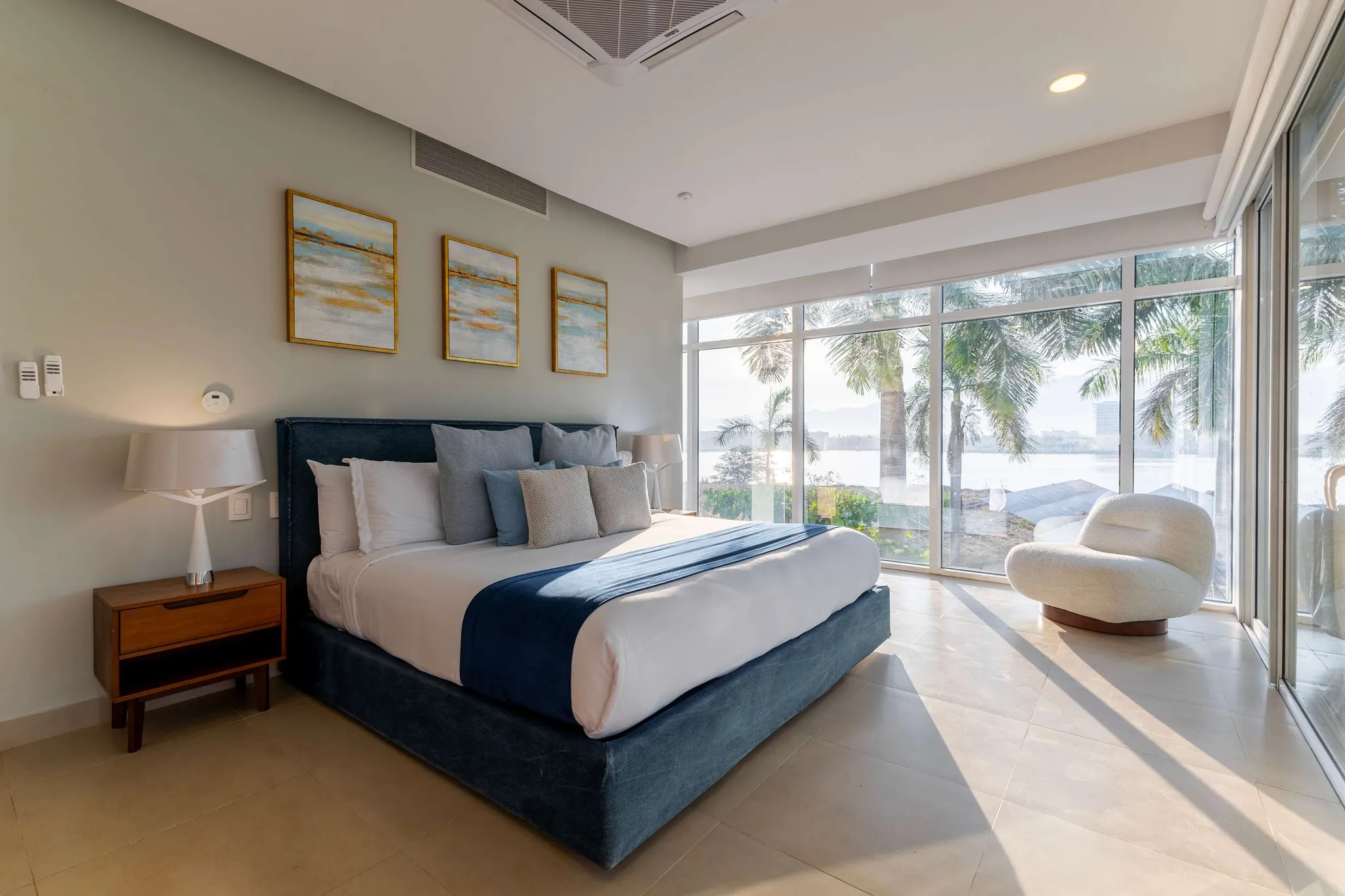 A serene bedroom with a king-sized bed, large windows, and a water view.