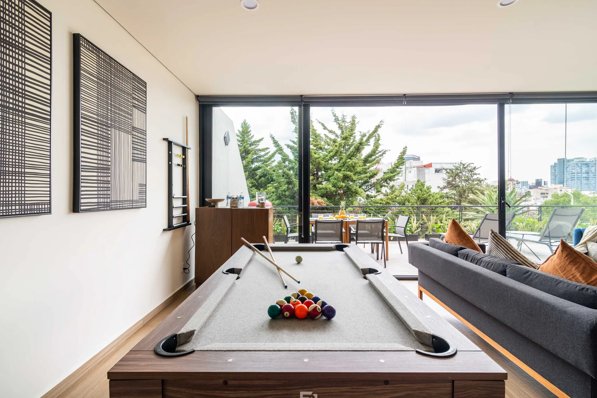 A modern living room with a pool table and large windows overlooking a city and trees.