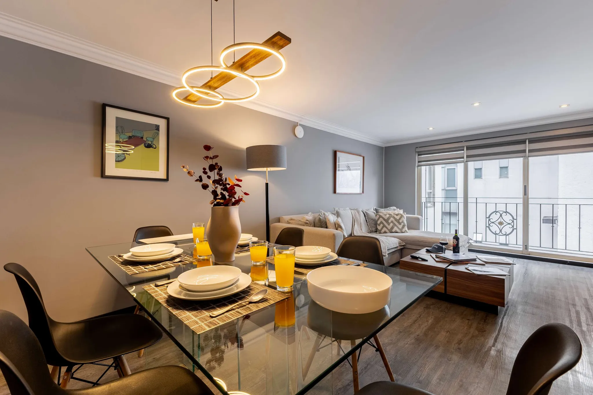 A dining room with a glass table set for four, surrounded by black chairs, and a sectional sofa in t