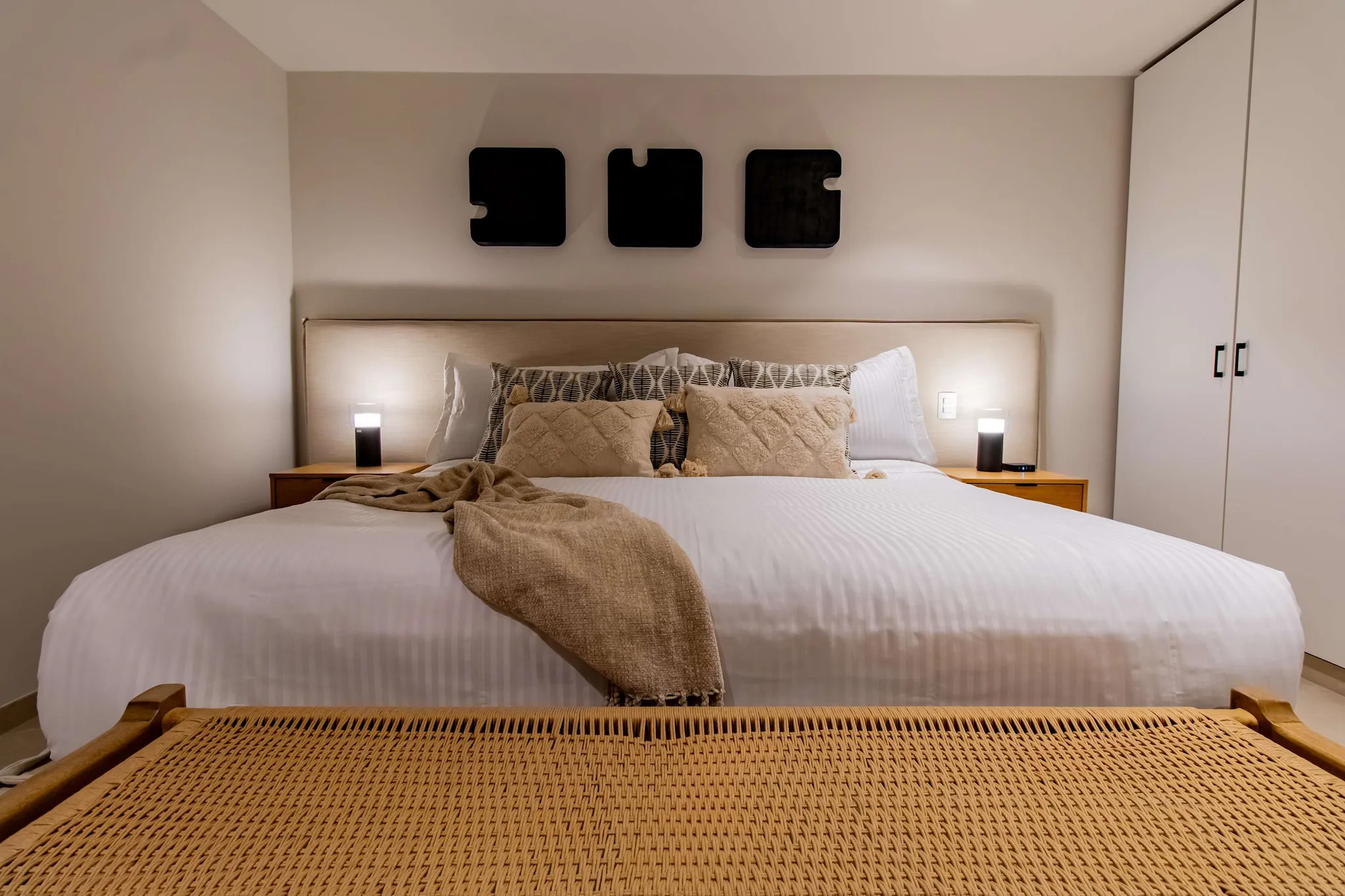 A modern bedroom with a large bed, bedside lamps, and decorative wall art.