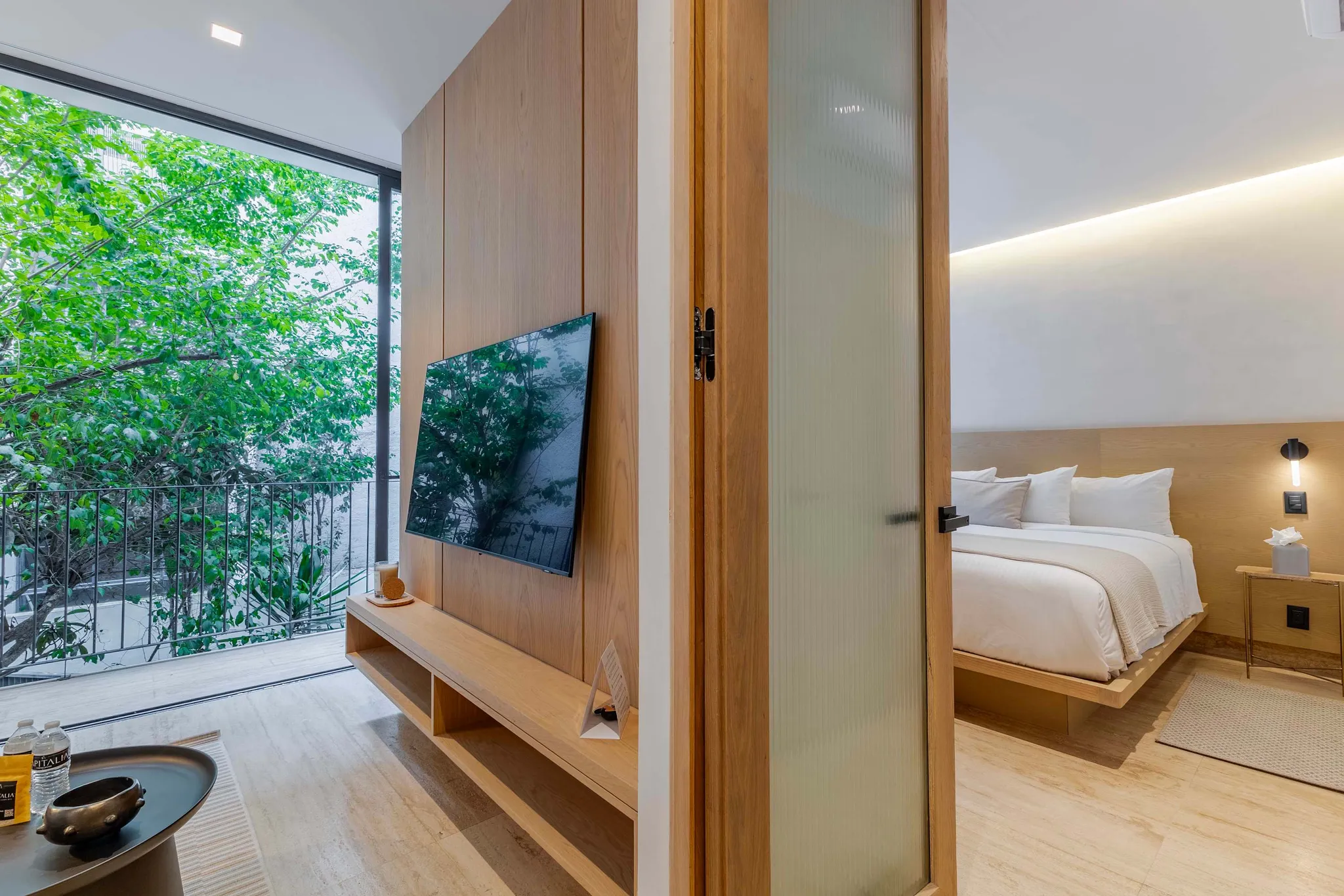 A bedroom with a bed and a TV visible through a doorway.