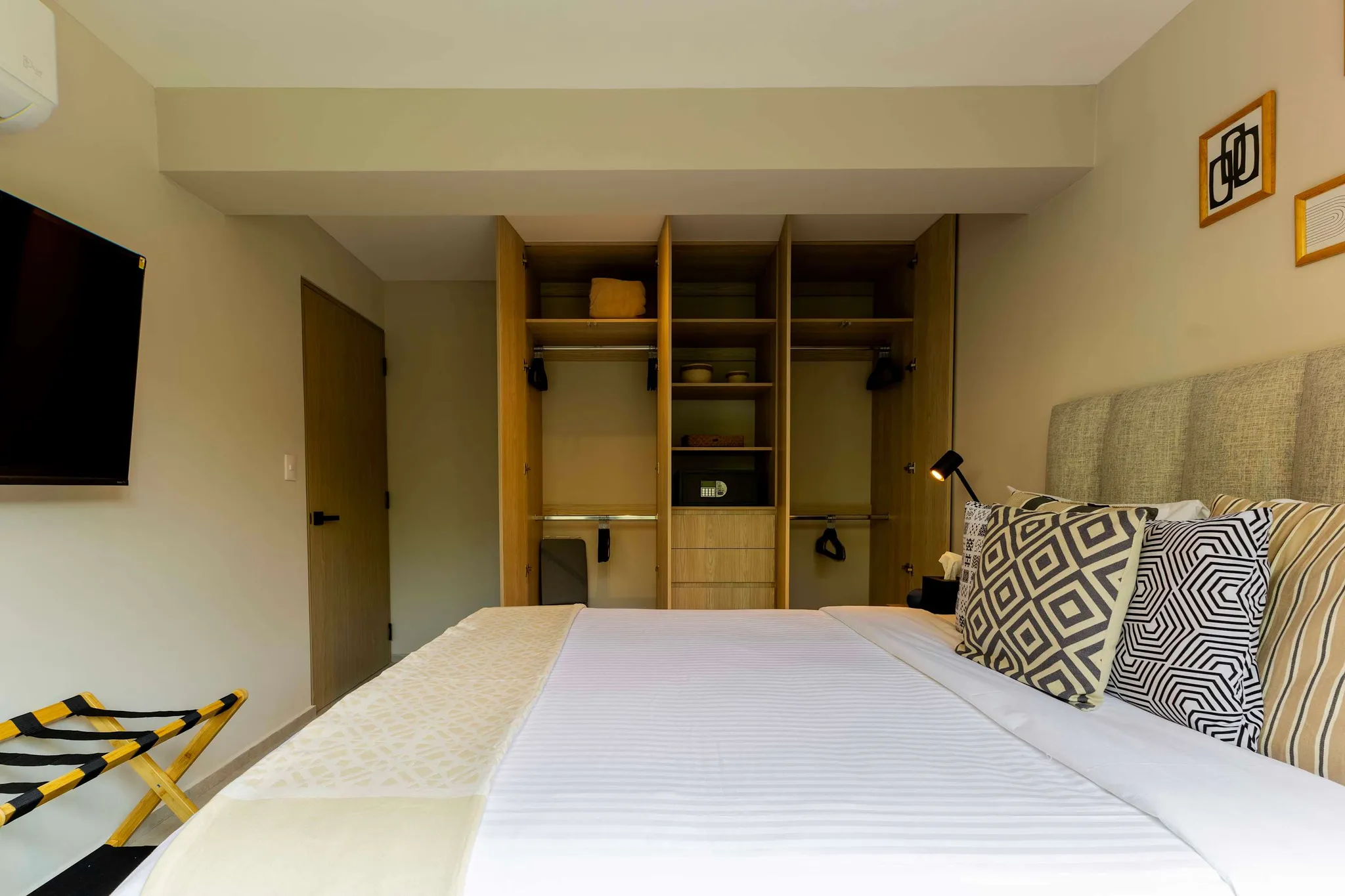 A bedroom with a TV, open closet, and a bed with patterned pillows.