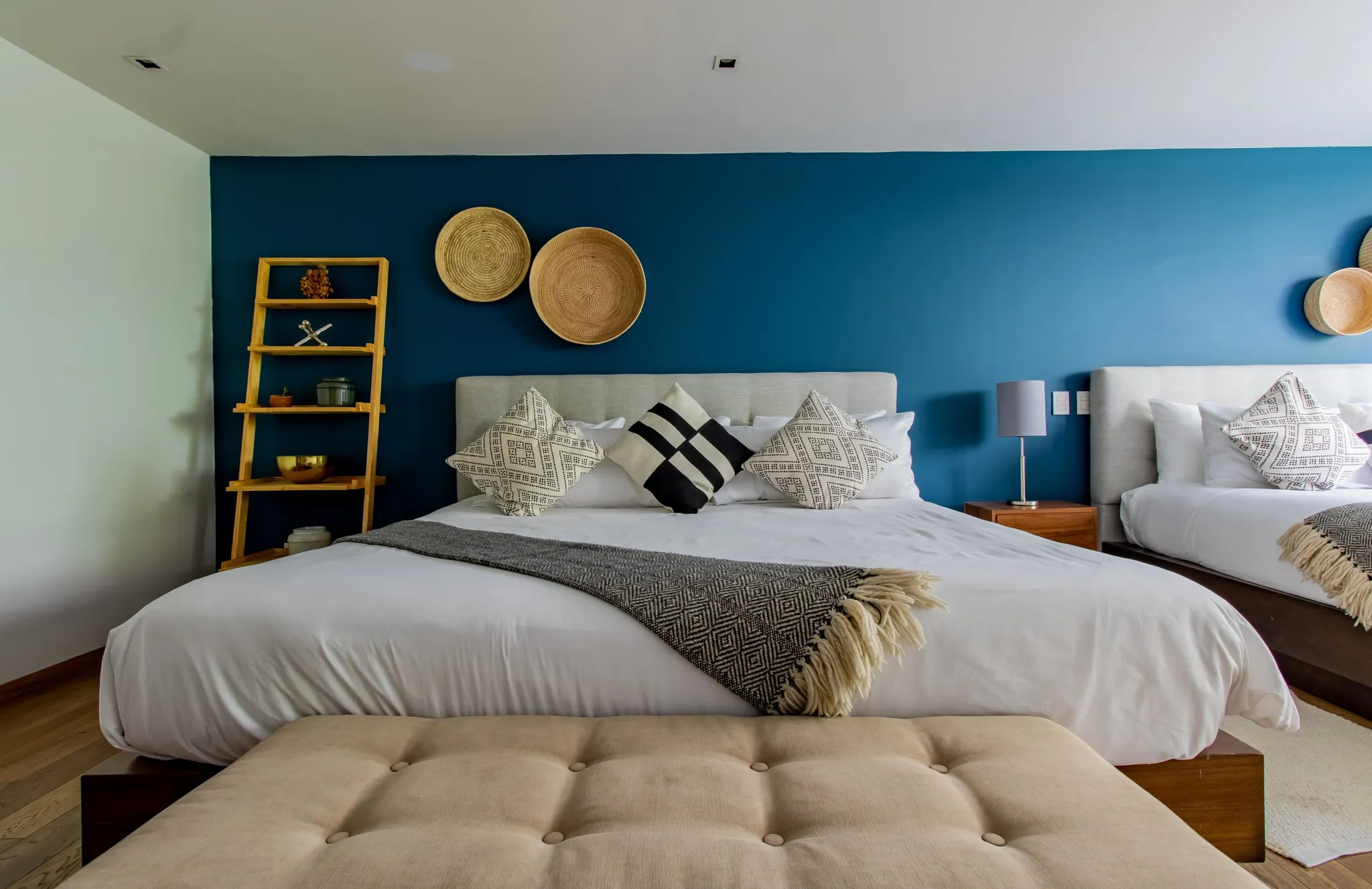 A minimalist bedroom with a queen bed, blue walls, and wooden accents.